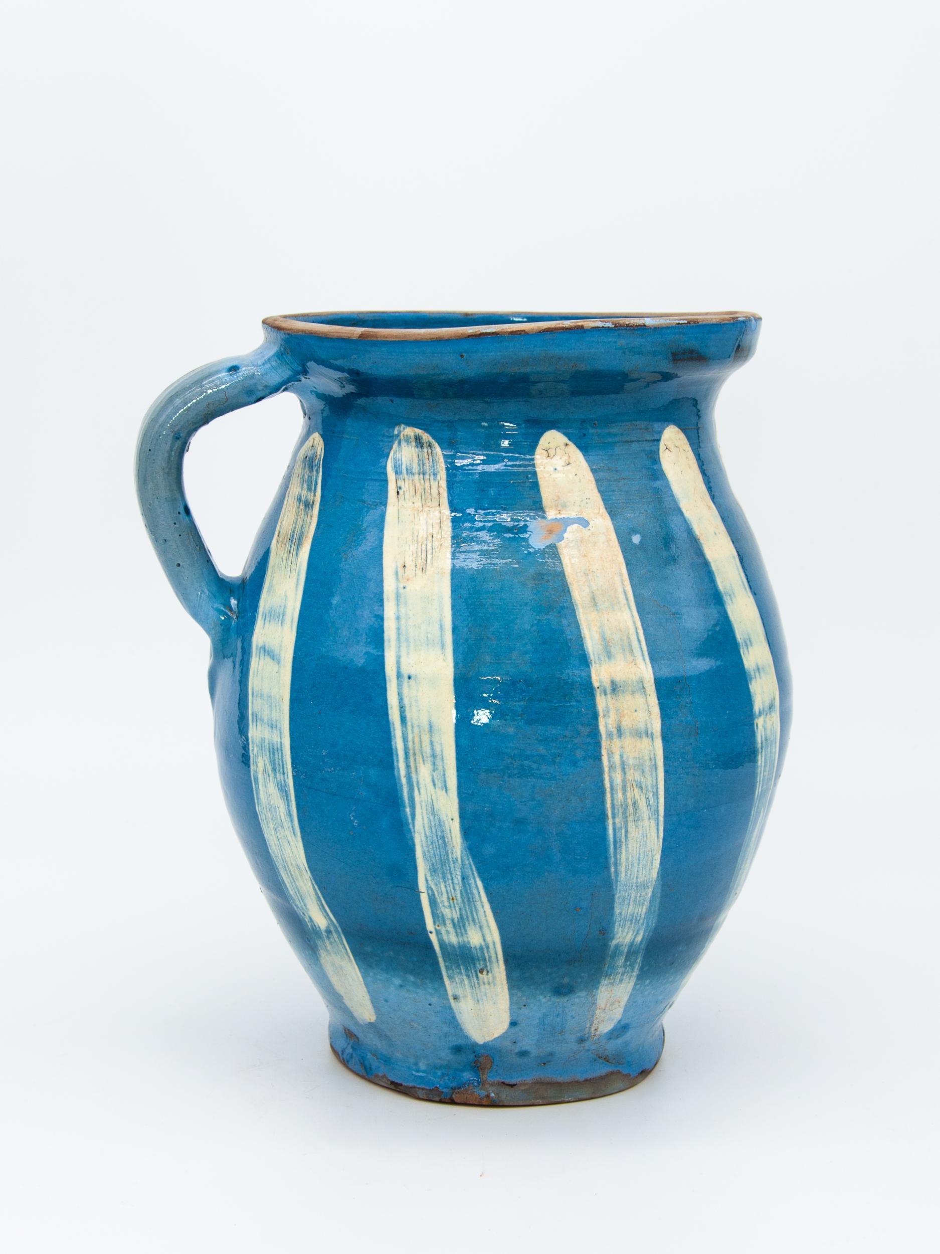 A handmade pitcher with blue glaze and white stripes. Classic blue and white in a rustic style is perfect for a country setting.