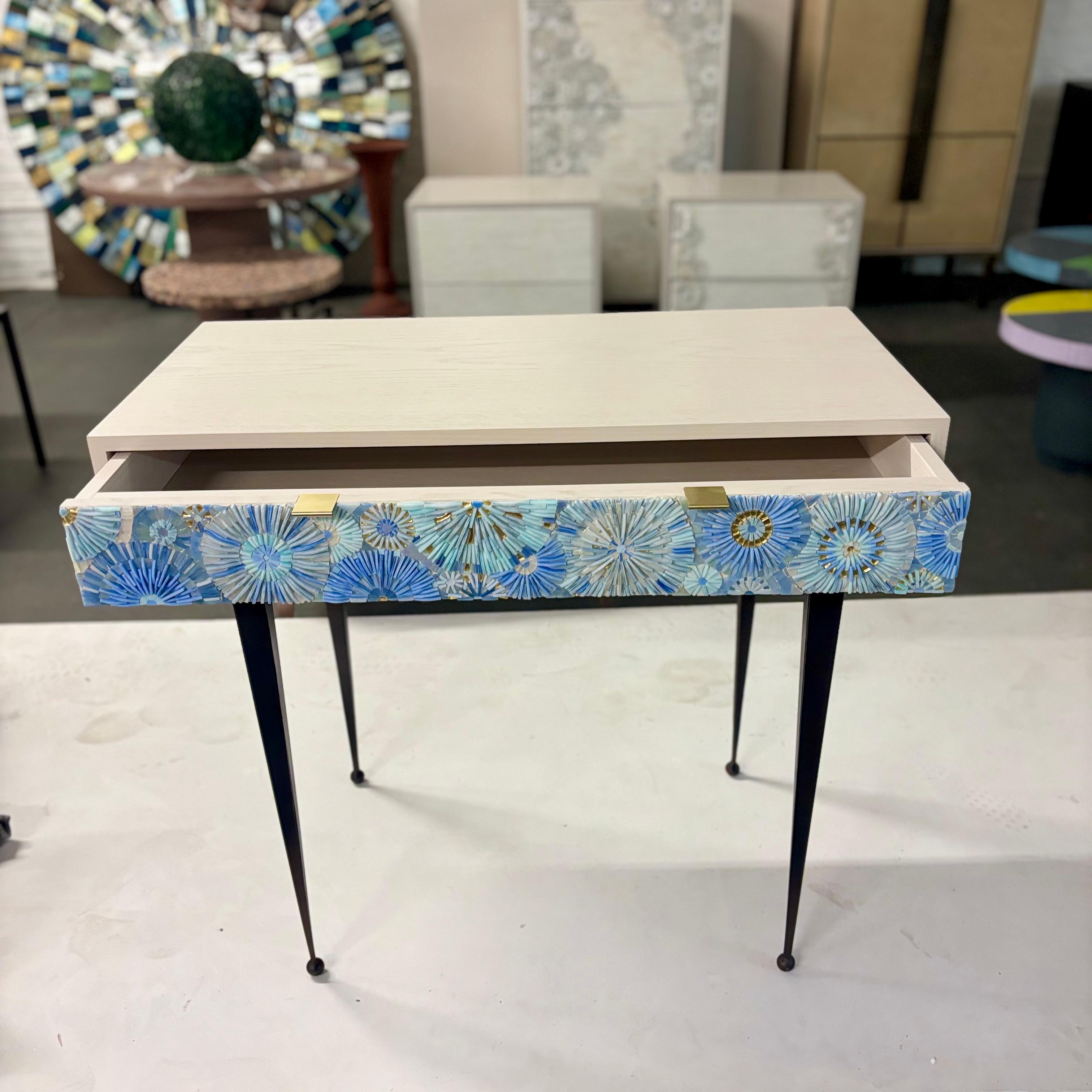 La scrivania Pavia Blossom di Ercole Home è dotata di un unico cassetto, con finitura Washed Ivory Dark su rovere. I mosaici in vetro tagliato a mano nei colori blu francese, blu cielo e oro decorano i frontali dei cassetti con un motivo a fiore.