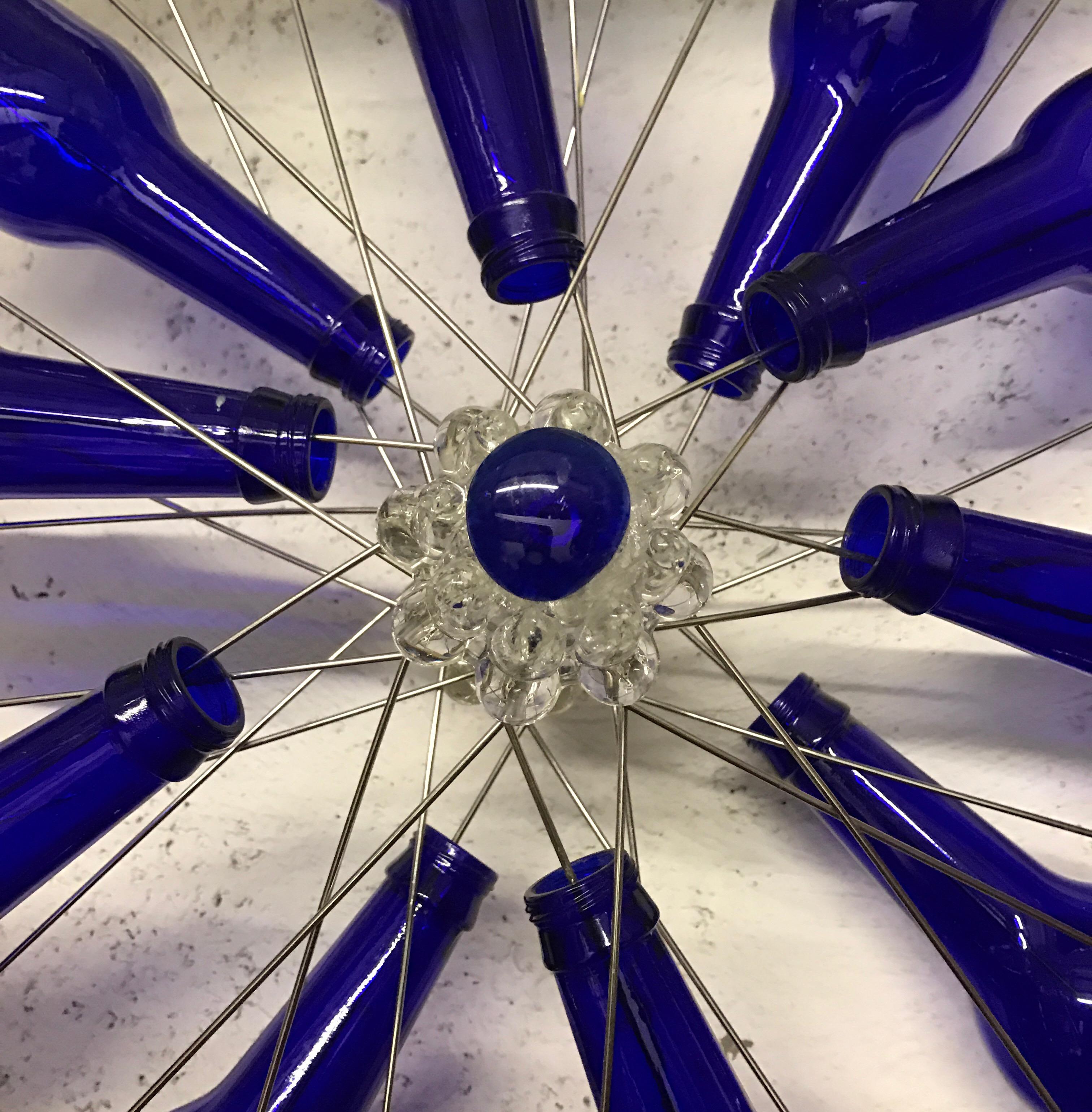 Modern blue bottles on a bike wheel sculpture
Blue bottles attached to the wheel of a bicycle and hand-wired further embellished with a blue ornament in the centre of the wheel.
Miami artist
Size: 25” diameter x 8” depth.