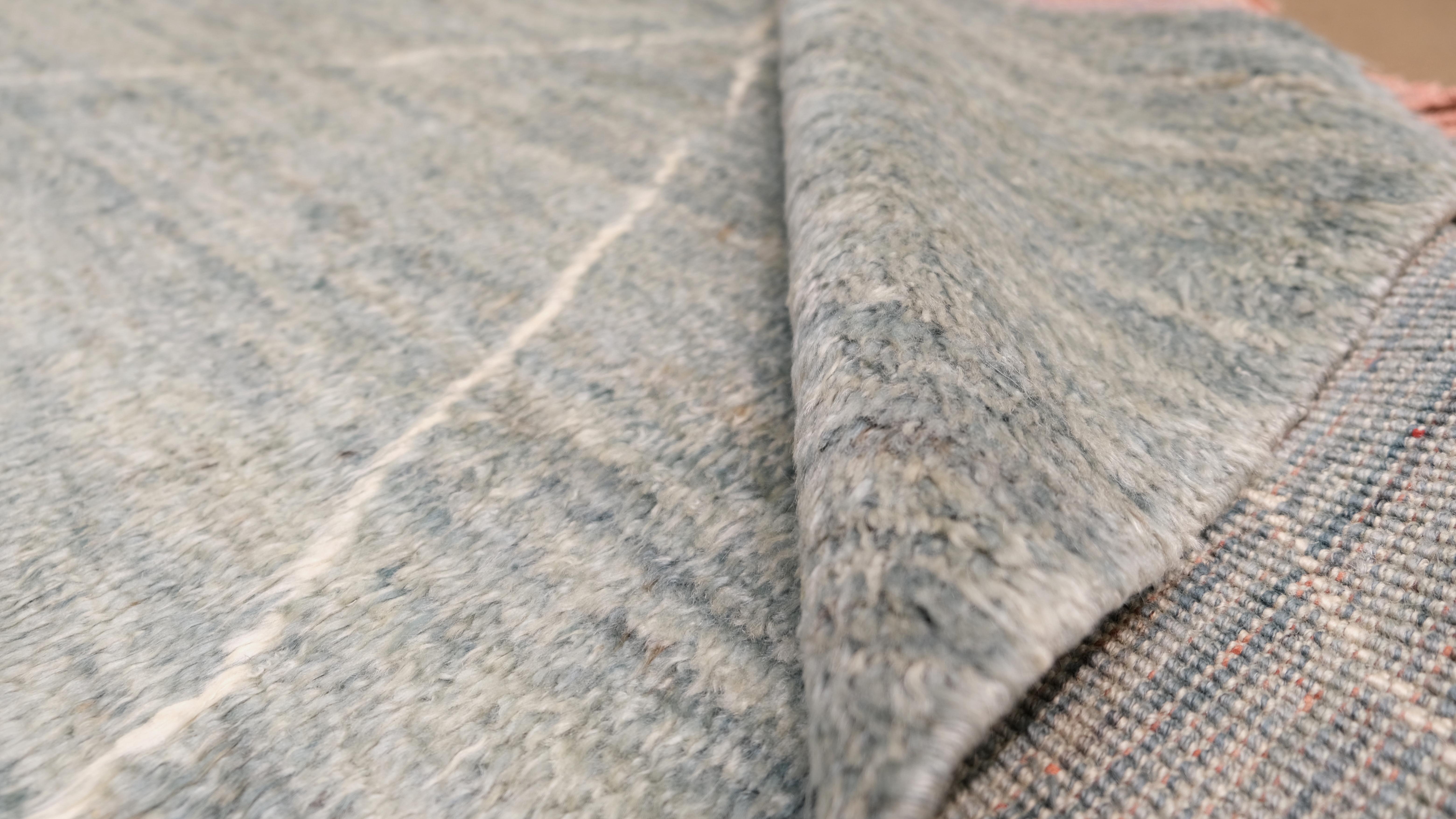 Introduce elegance and warmth to your home with this hand-knotted wool rug. Inspired by traditional Moroccan designs, this rug features a delicate diamond pattern in soft neutral tones of grey blue green, and Ivory complemented by charming fringed