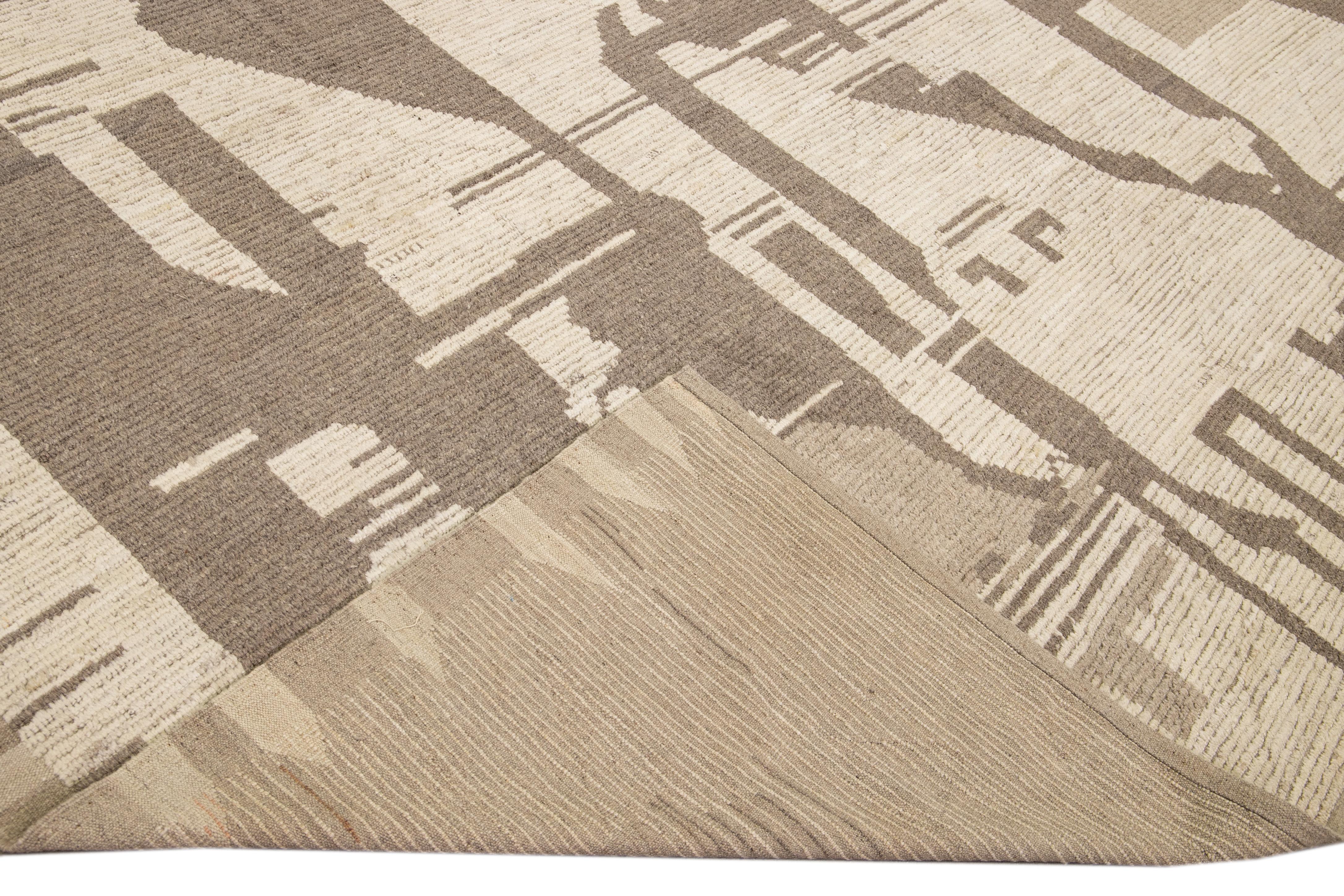Preciosa alfombra de lana hecha a mano de estilo marroquí con un campo beige. Esta moderna alfombra tiene detalles en marrón, amarillo y azul y un precioso diseño abstracto integral.

Esta alfombra mide 13'7