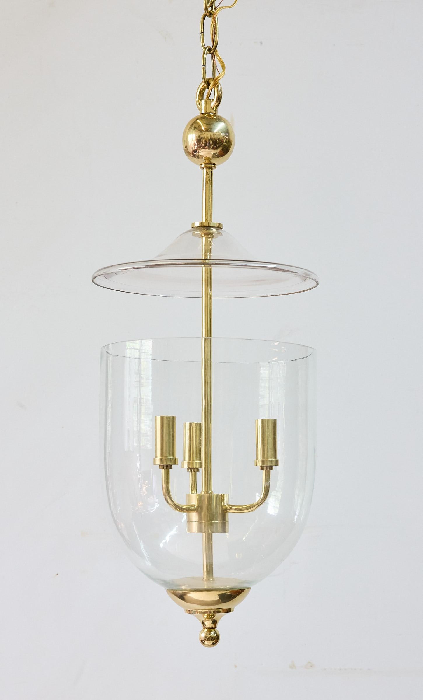 Lanterna contemporanea in stile georgiano dalla tradizionale forma a campana con linee morbide e moderne. Un classico contenitore in vetro contiene tre candelabri, mentre un paralume in vetro è sospeso sopra, il tutto sostenuto da una barra centrale