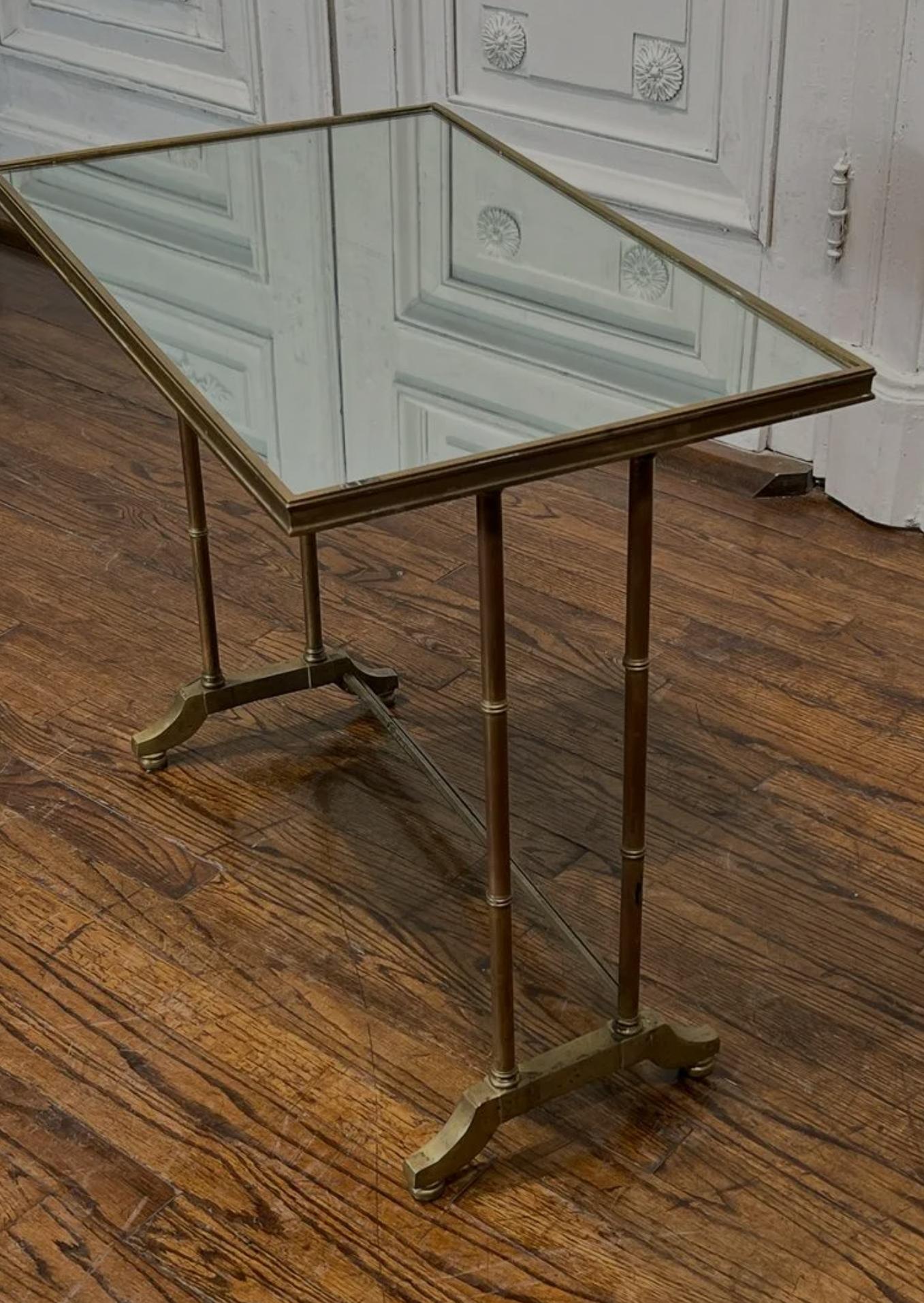 A Modern bronze mirrored side table, second half of 20th century, having a rectangular mirror tabletop, rising on faux bamboo supports, resting on trestle base.

Dimensions: (approx)
23.25