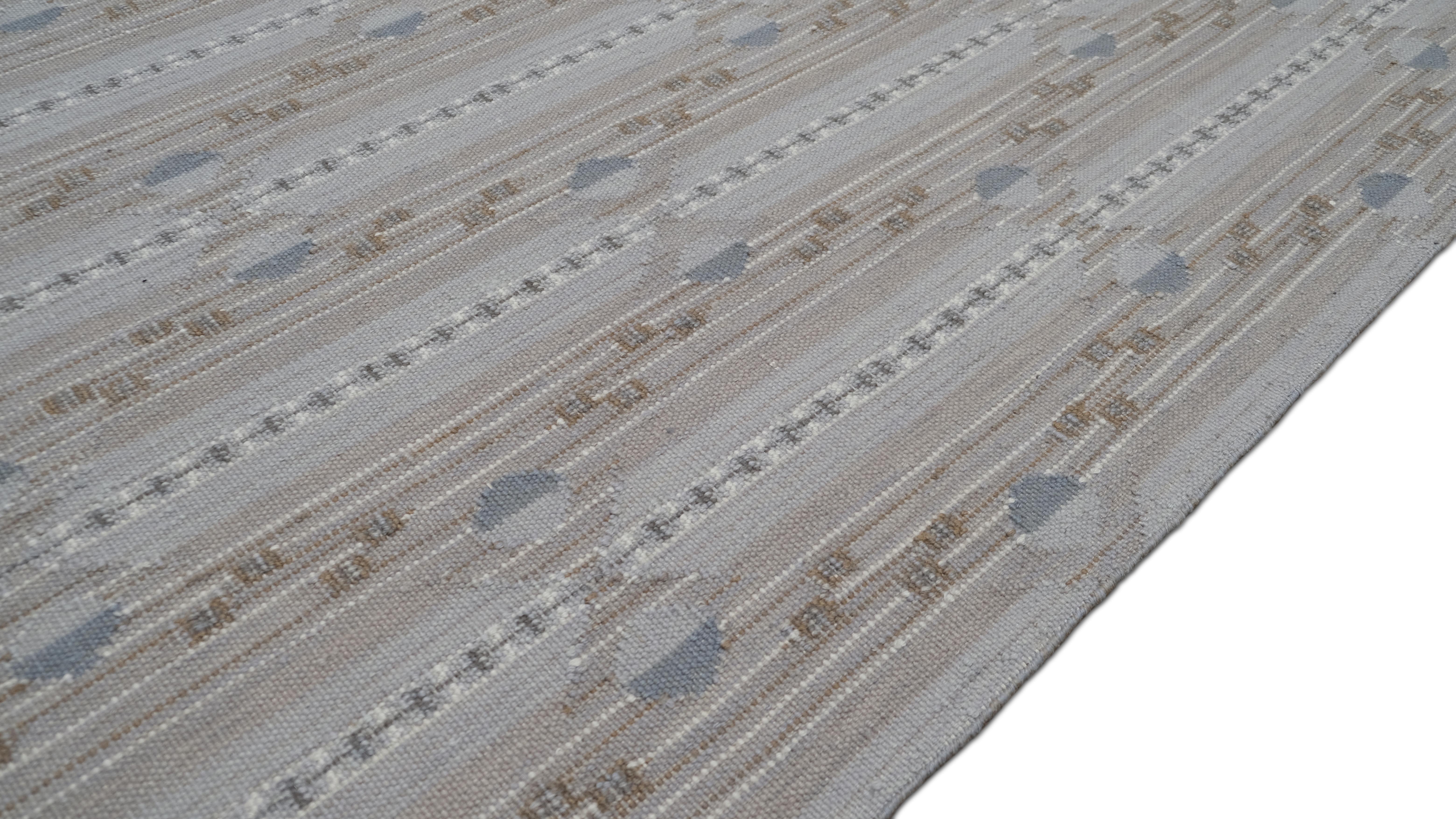Eleganza raffinata con questo tappeto in lana intrecciata a mano, disegnato con un delicato motivo geometrico a righe che emana una raffinatezza sottile. La palette di colori neutri, con sfumature di blu, marrone e grigio tenue, garantisce