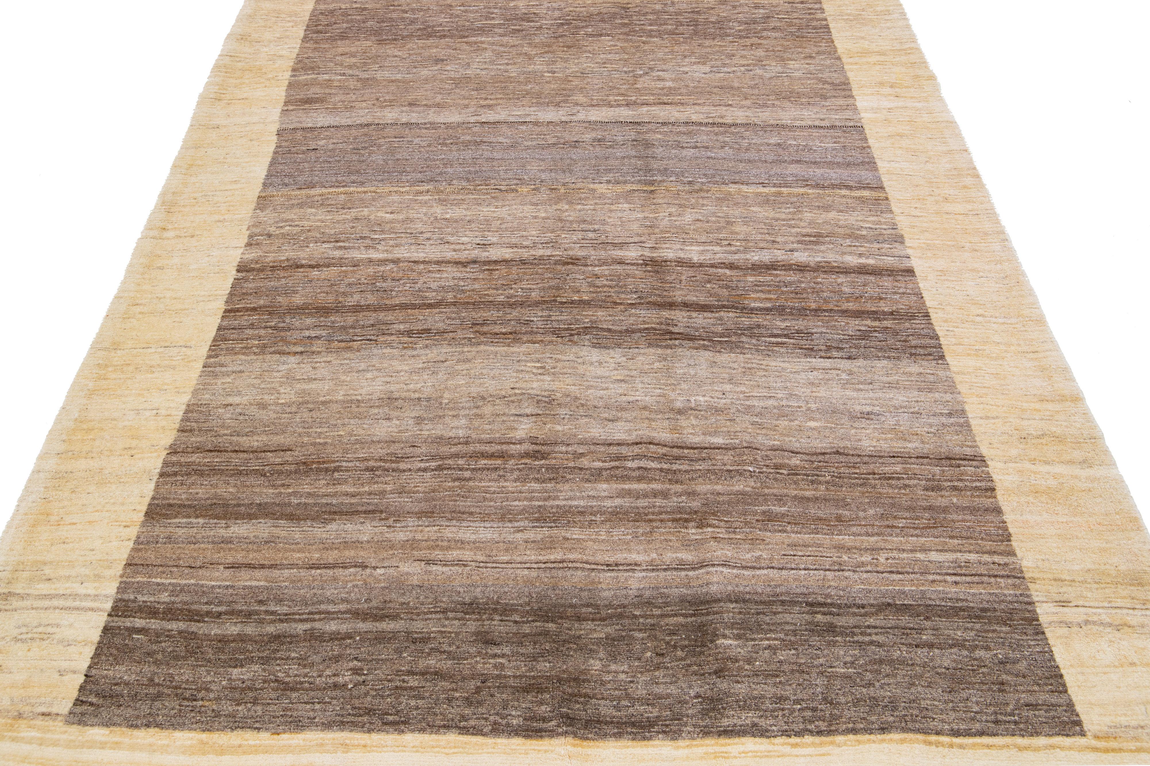 Magnifique tapis moderne en laine tissée à la main de style Gabbeh, avec un champ de couleur marron. Cette pièce a des accents beiges dans un magnifique design minimaliste.

Ce tapis mesure : 5'8