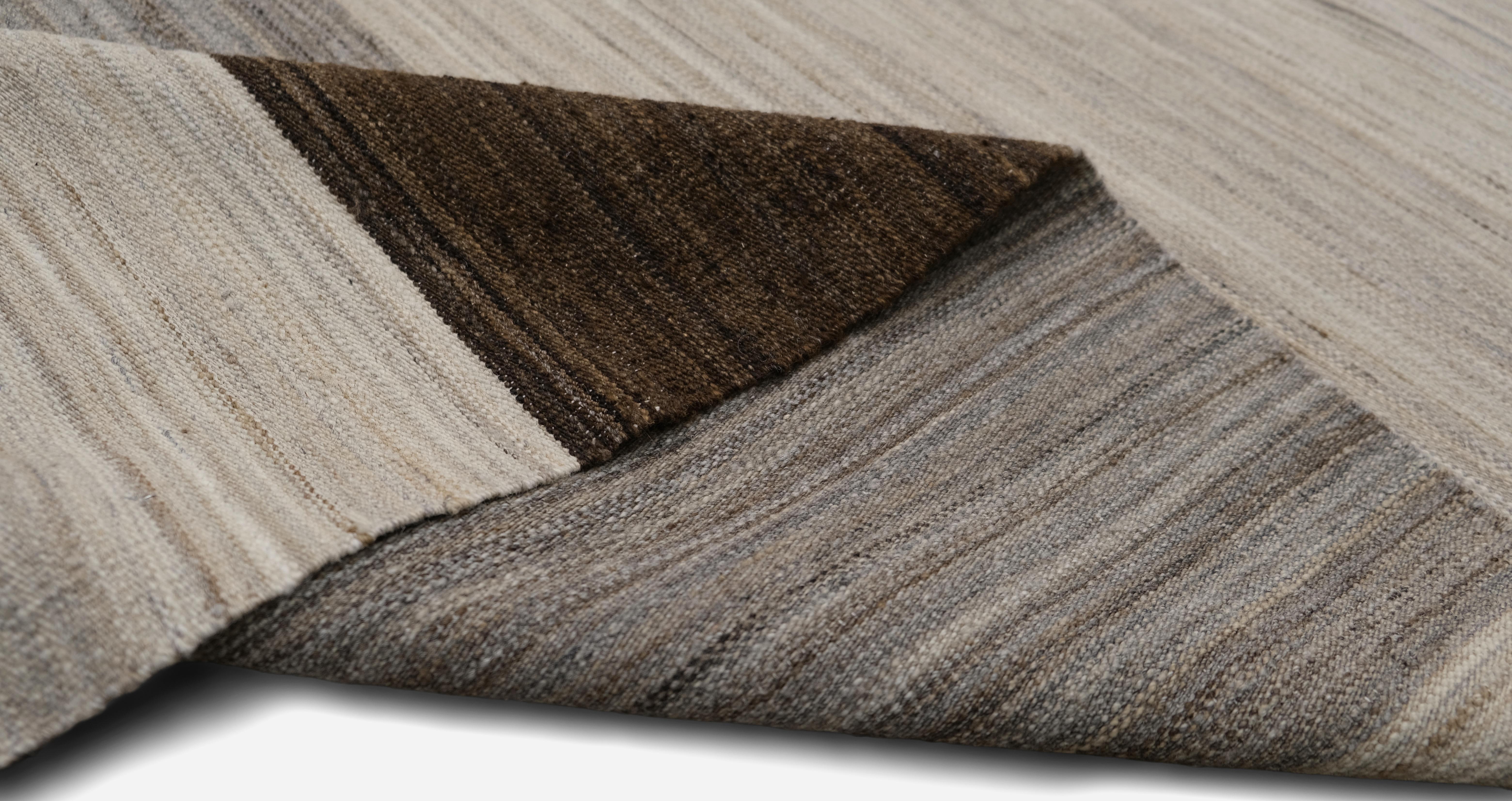 Ce tapis en laine tissé à la main présente un motif rayé sophistiqué dans des tons naturels, mêlant l'ivoire, le marron et le gris pour une esthétique intemporelle et moderne. La variation subtile des couleurs et des textures met en valeur la beauté