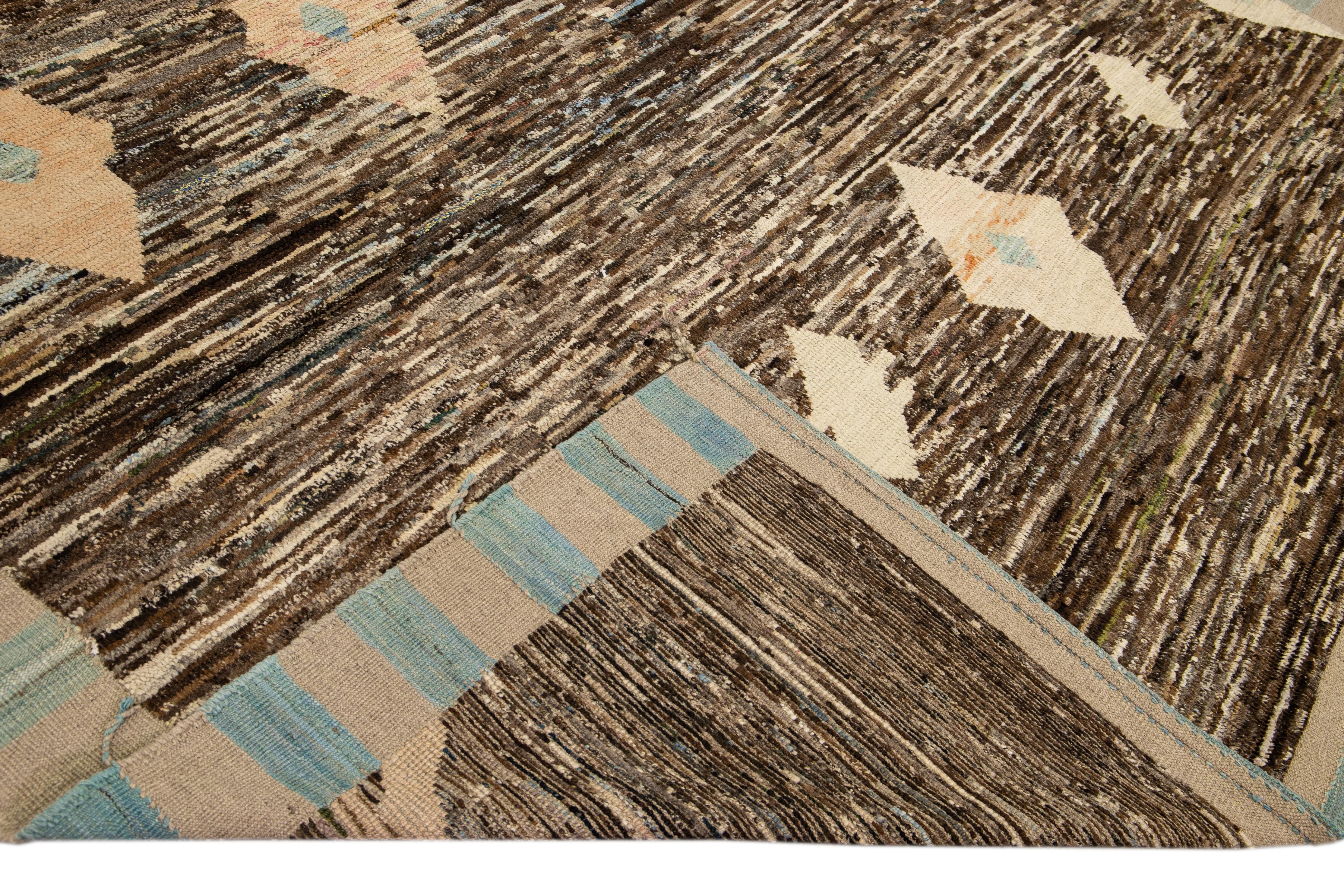 Magnifique tapis en laine fait main de style marocain avec un champ brun. Ce tapis moderne aux accents pêche et beige et aux franges tressées beige-bleu présente un superbe motif géométrique bohème sur toute sa surface.

Ce tapis mesure : 9'9