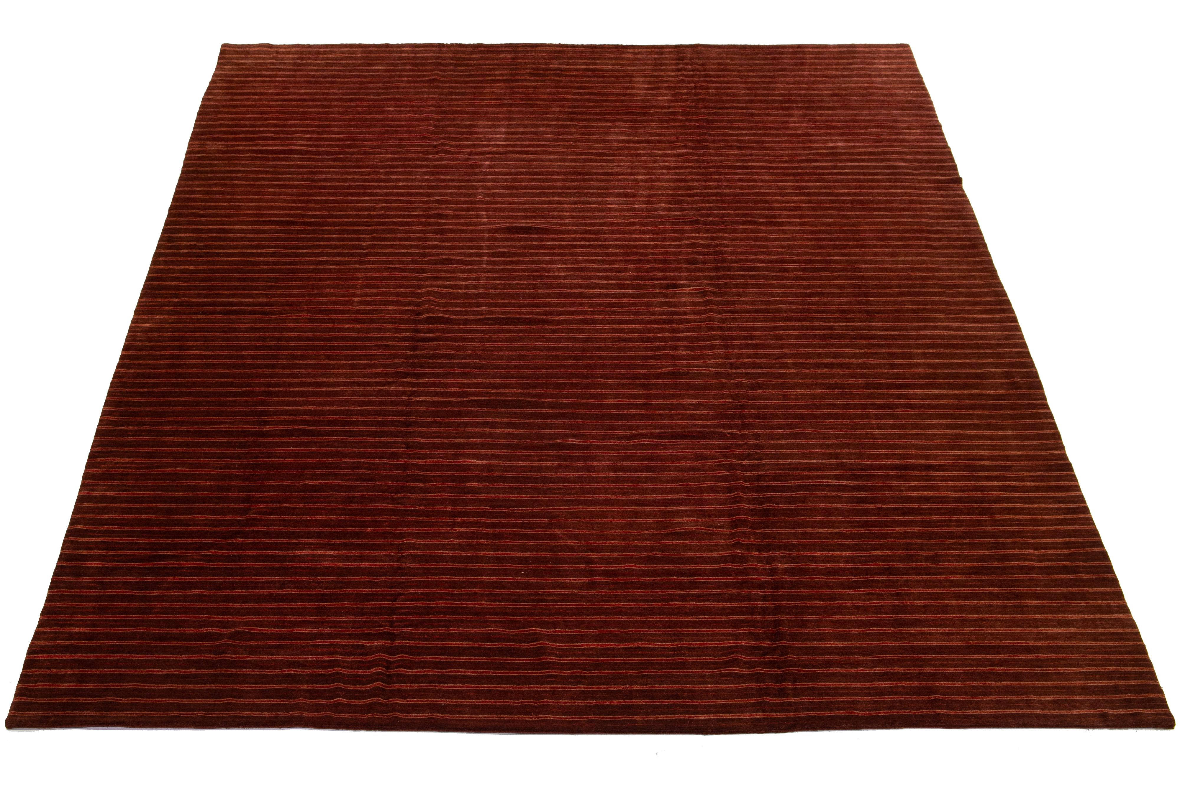 Dieser moderne tibetische Teppich hat einen burgunderroten Hintergrund mit rostfarbenen Akzenten, wodurch ein schickes und raffiniertes Streifendesign entsteht, das die Essenz des Modernismus im 21. Jahrhundert widerspiegelt.

Dieser Teppich misst