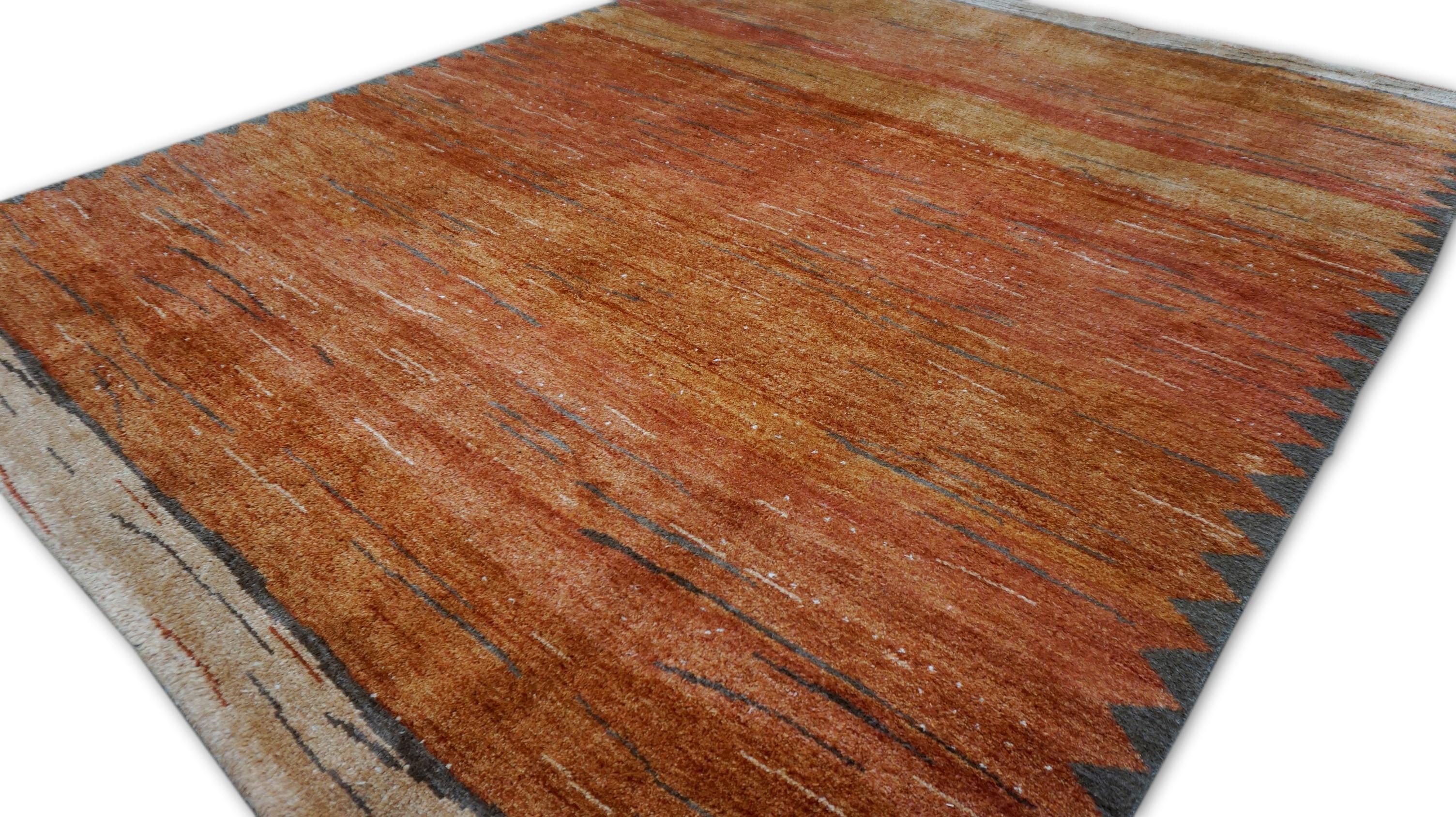 Ce tapis en laine nouée à la main en Inde illustre le savoir-faire artisanal moderne avec une approche minimaliste mais texturée. Le tapis présente un champ orange brûlé chaud accentué par des stries horizontales panachées de couleur tan et