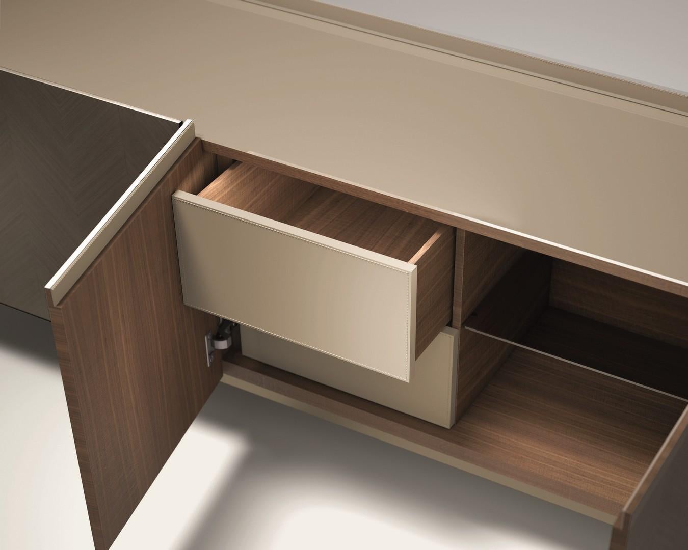 Si tratta di una credenza dalla linea pulita, rivestita con intarsi geometrici in legno pregiato. È disponibile nei colori Tay chiaro, Tay scuro e Noce canaletto. Piano con contenitore disponibile in vetro verniciato, marmo e Wood. Profilo superiore