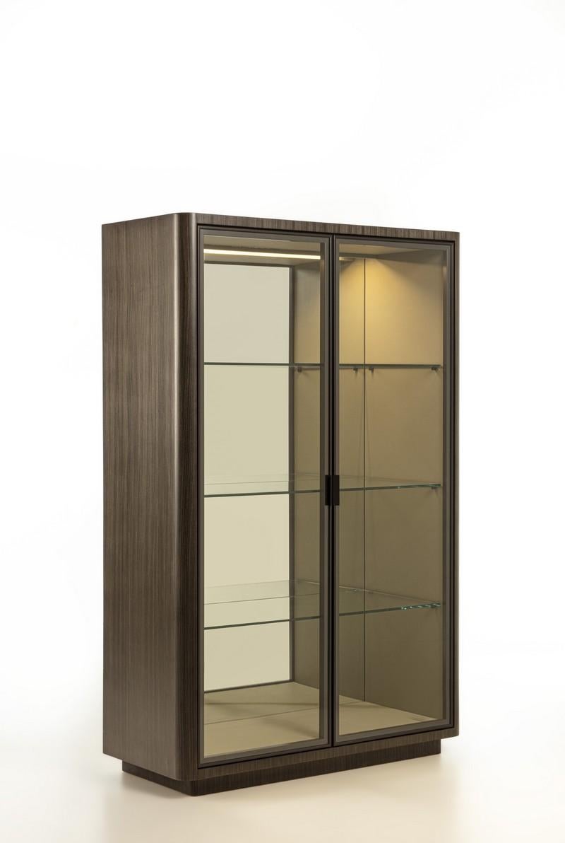 Showcase with elegant linear design. The exterior structure is embellished with dark Tay (VE49B) upholstery and rounded corner detail. The interior features fine details, leather-covered interior structure, mirrored back and aluminum profile doors.