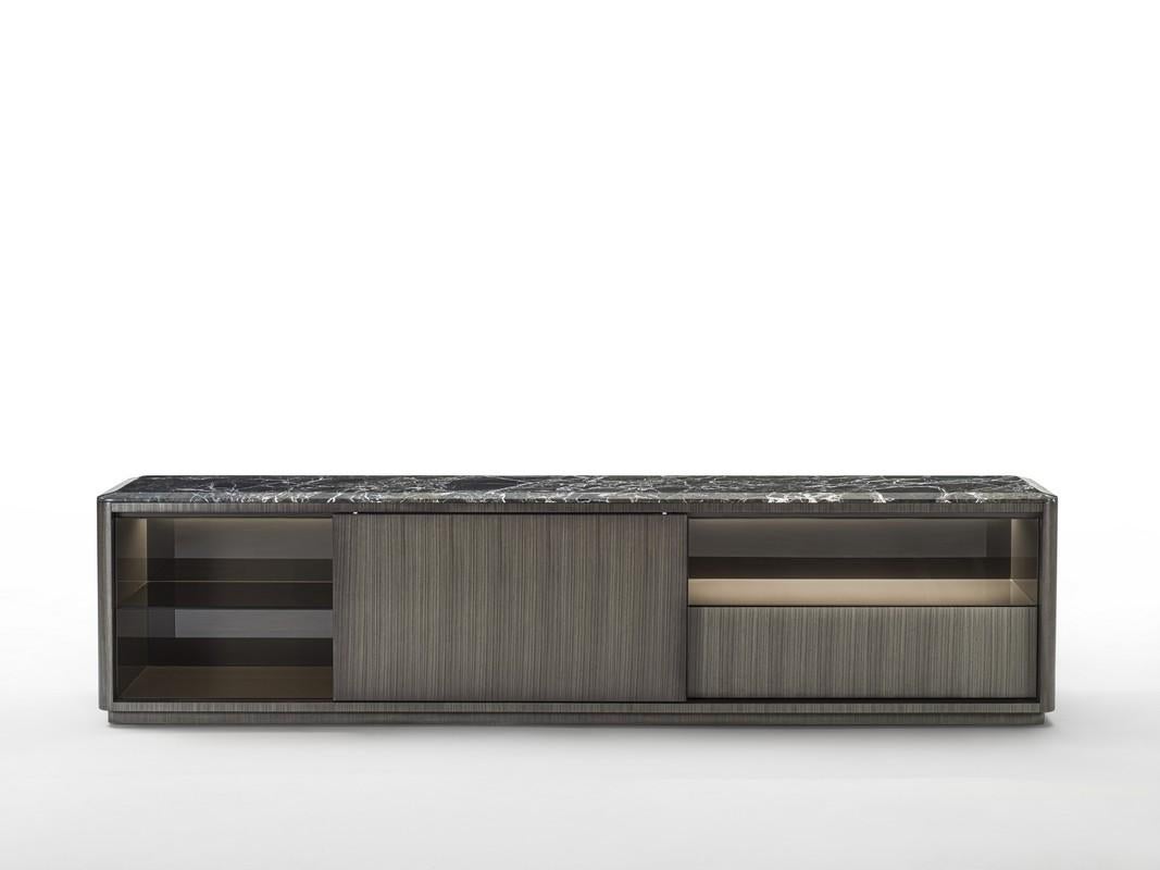 Sideboard characterized by the linear design, embellished by the dark Tay (CR77B) upholstered frame and the detail of rounded corners. The sliding door creates multiple compositions with open and drawer compartments. The internal structure of the