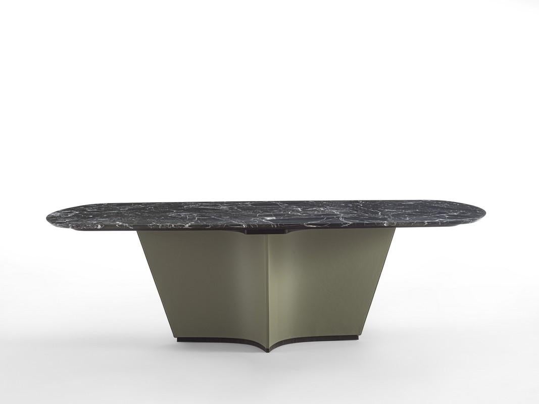 Table avec base sculpturale en forme de croix, entièrement recouverte de cuir. Le plateau en marbre vert Lepanto FM08B est chanfreiné à la base, le profil de la base est en Tay scuro (TA73B), également disponible en Tay Chiaro (TA73C) et Noce