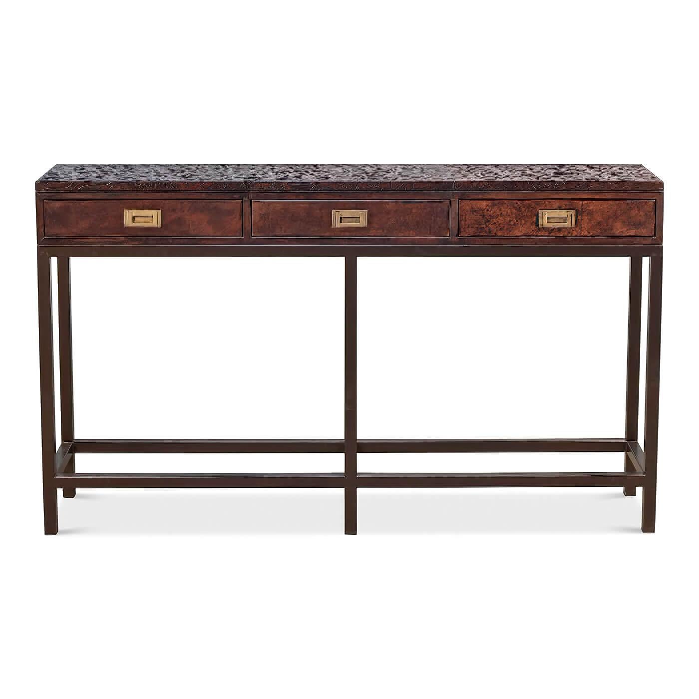 A modern campaign-style console table with an embossed leather top. This three-drawer console is accented with brass campaign-style hardware and sits on a metal base. 

Dimensions: 60