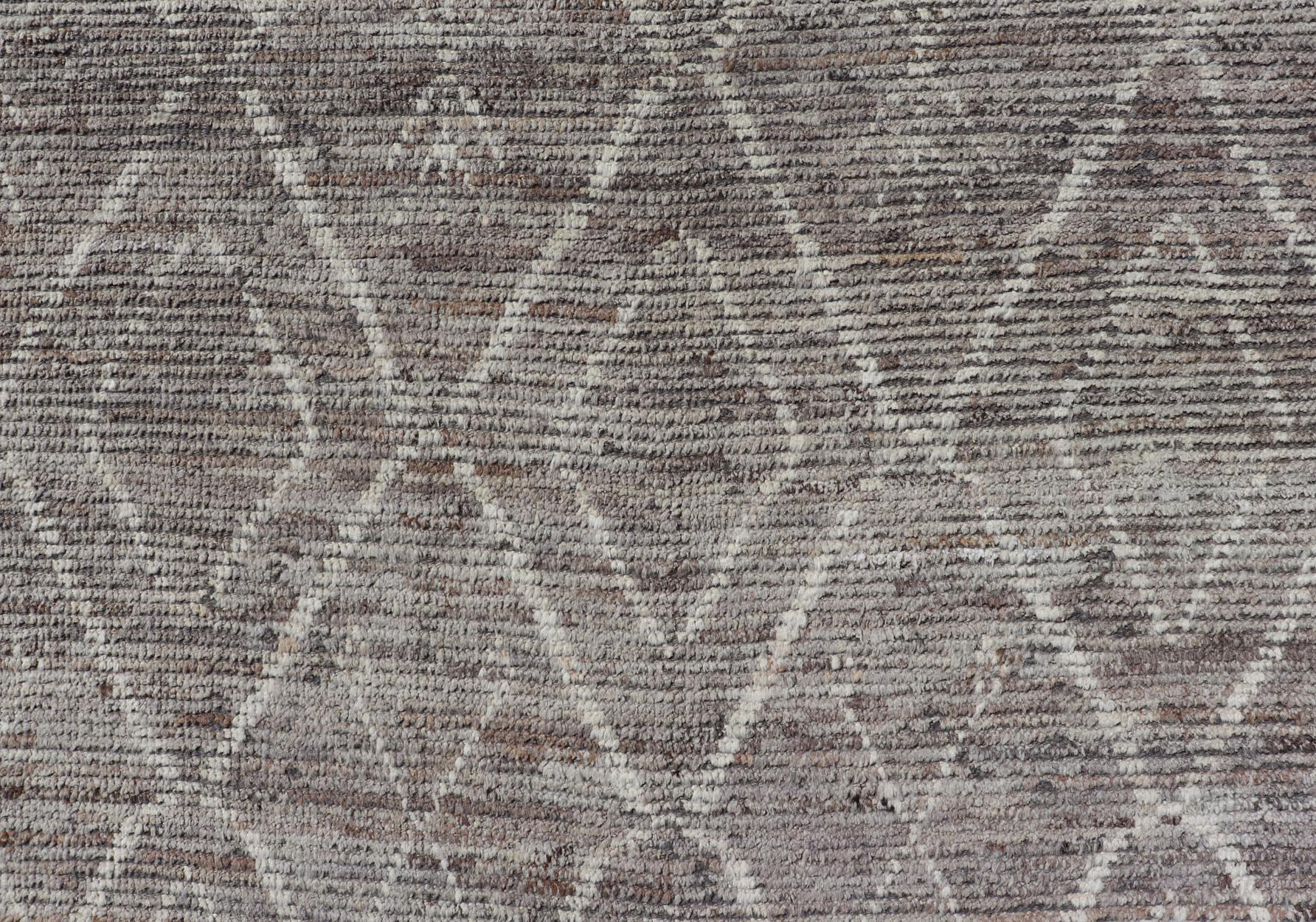 Ce tapis moderne et décontracté a été noué à la main. Le tapis présente un motif géométrique marocain en diamants, agrémenté de divers motifs gris et crème, ce qui fait de ce tapis un superbe choix pour une variété d'intérieurs classiques, modernes,