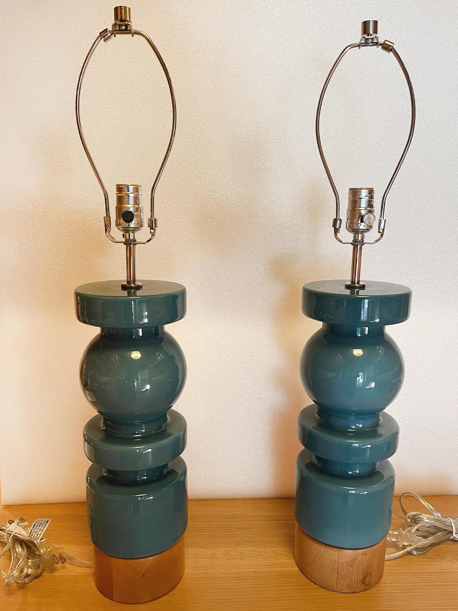 A beautiful pair of ceramic table lamps with beech wood bases and chrome hardware. They are in a teak blue glaze and have a columnar form that combine ball and cylindrical shapes. 

Dimensions:
29 in. overall height to finial
16 in. lamp body