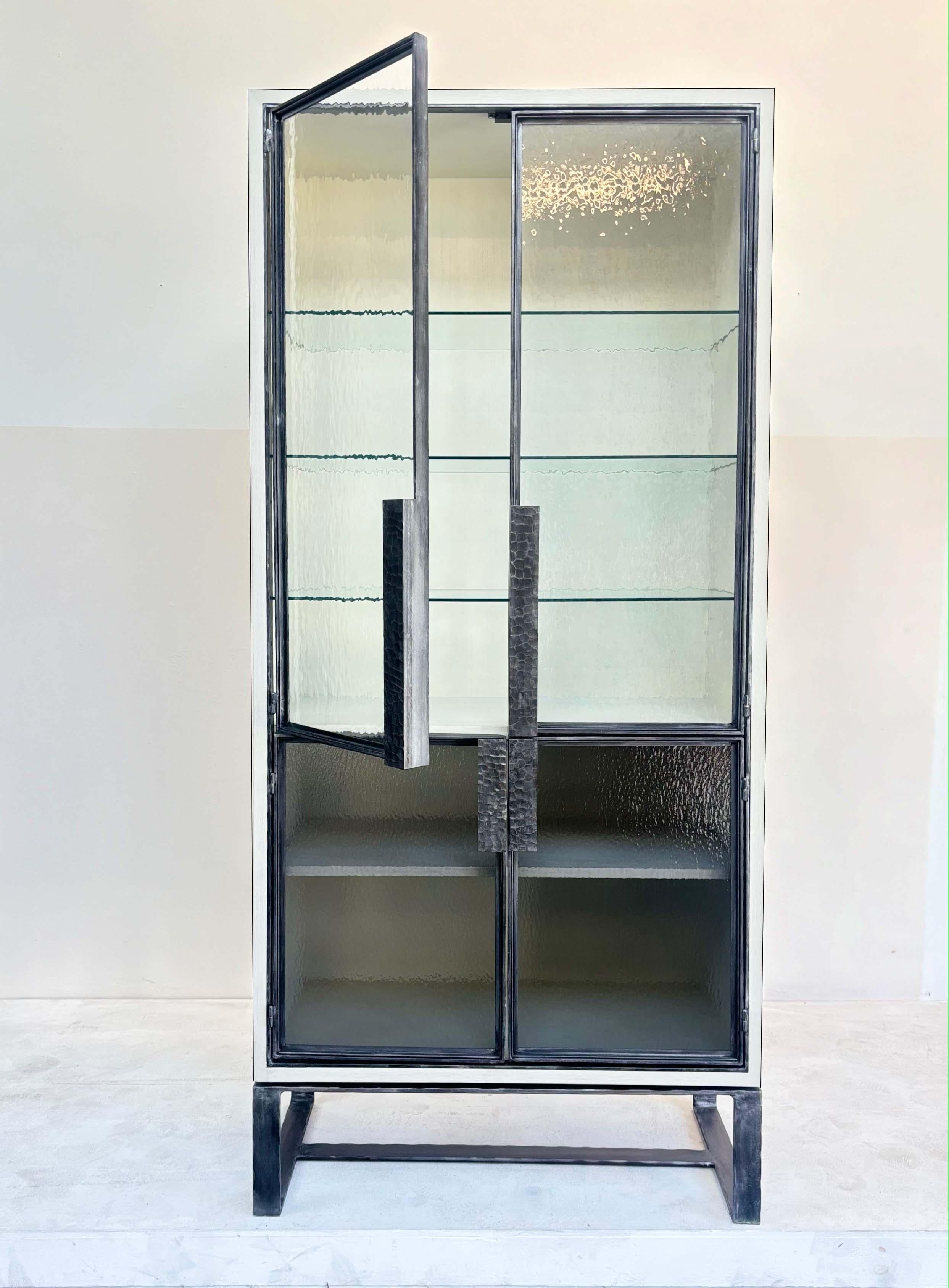 La Vitrine 4 portes en verre d'eau Modern Chelsea d'Ercol est composée d'une combinaison unique de verre d'eau taillé à la main et de métal martelé à la main. Les quatre portes sont encadrées de métal étain, avec des poignées martelées à la main. 