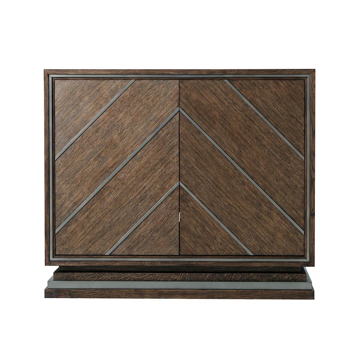 A modern Chevron design cabinet with brushed quarter oak veneer in our Charteris finish, two doors with matte tungsten finish chevron overlays enclosing two adjustable shelves and raised on a stepped inset base. 

Dimensions: 40
