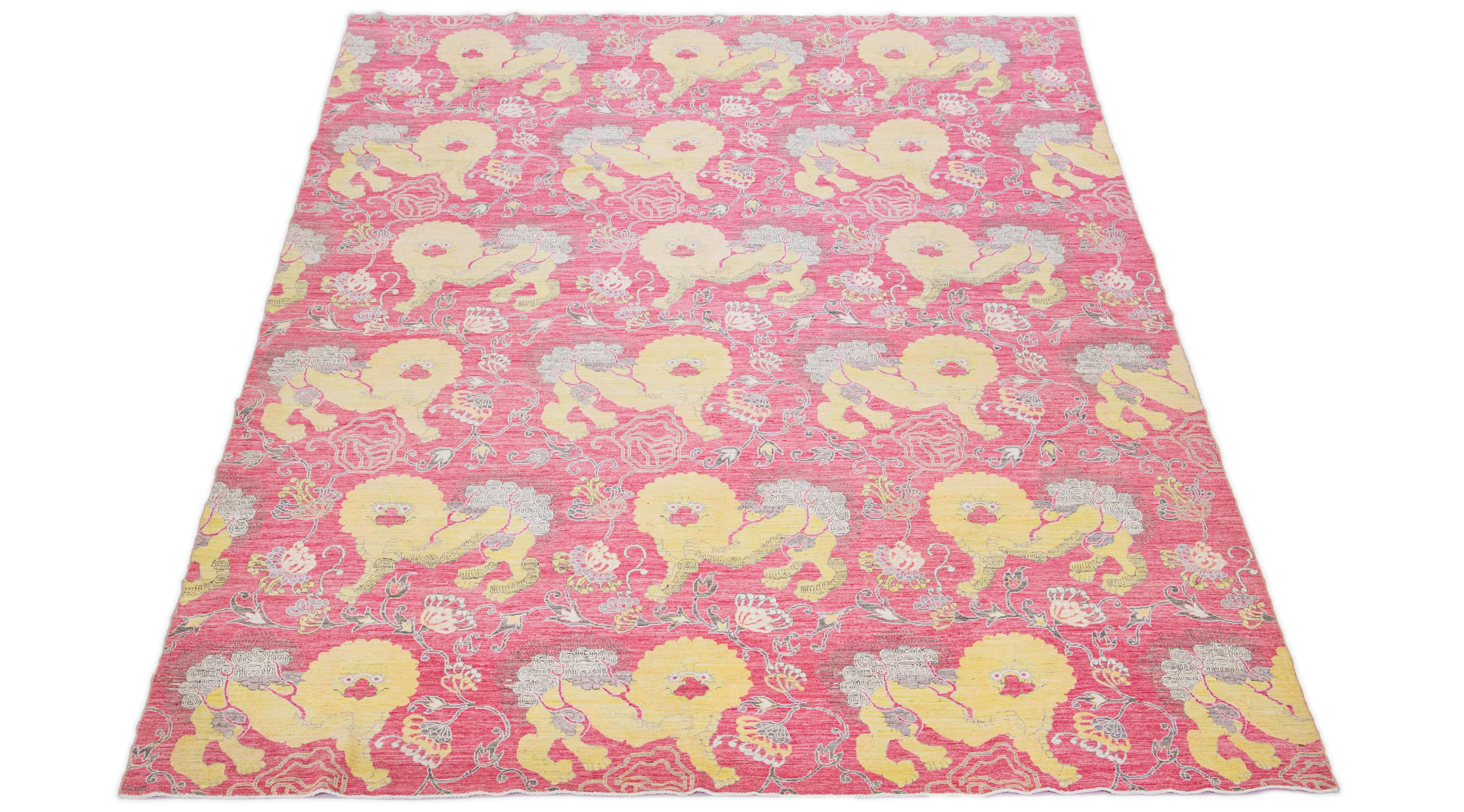 This hand-knotted wool rug showcases an exquisite Modern Art Deco design with a rich pink field accentuated by broad yellow and gray hues. The intricate Chinese-style foo dogs are beautifully depicted throughout the rug, embellished with