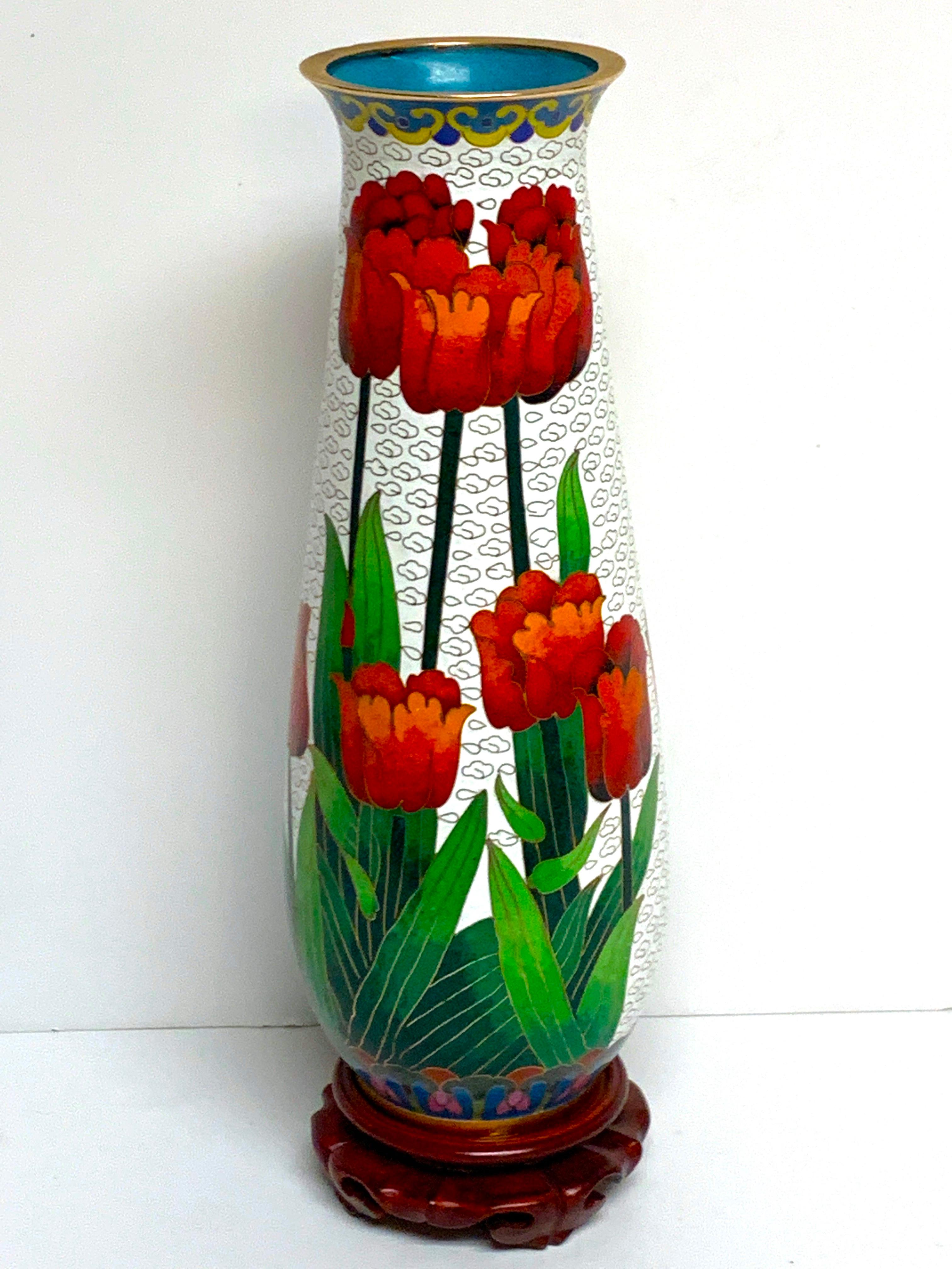 Modern Chinese Cloisonné tulip motif tapered vase and stand, beautifully enamelled with red tulips and white background, complete with carved hardwood stand.
The vase stands 10