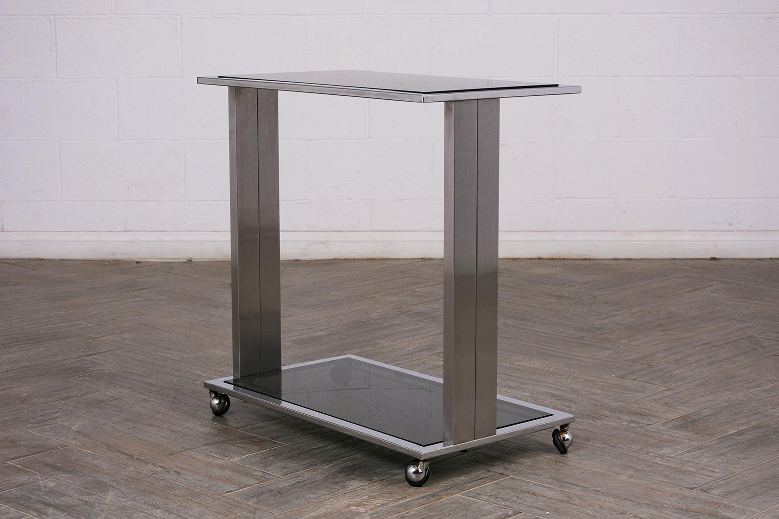 This modern style bar cart has a new chrome frame and is in good condition. The cart has two tiers and features two new smoke glass inserts. It has caster wheels which are in good working condition. This bar cart is sleek, elegant, and ready to be