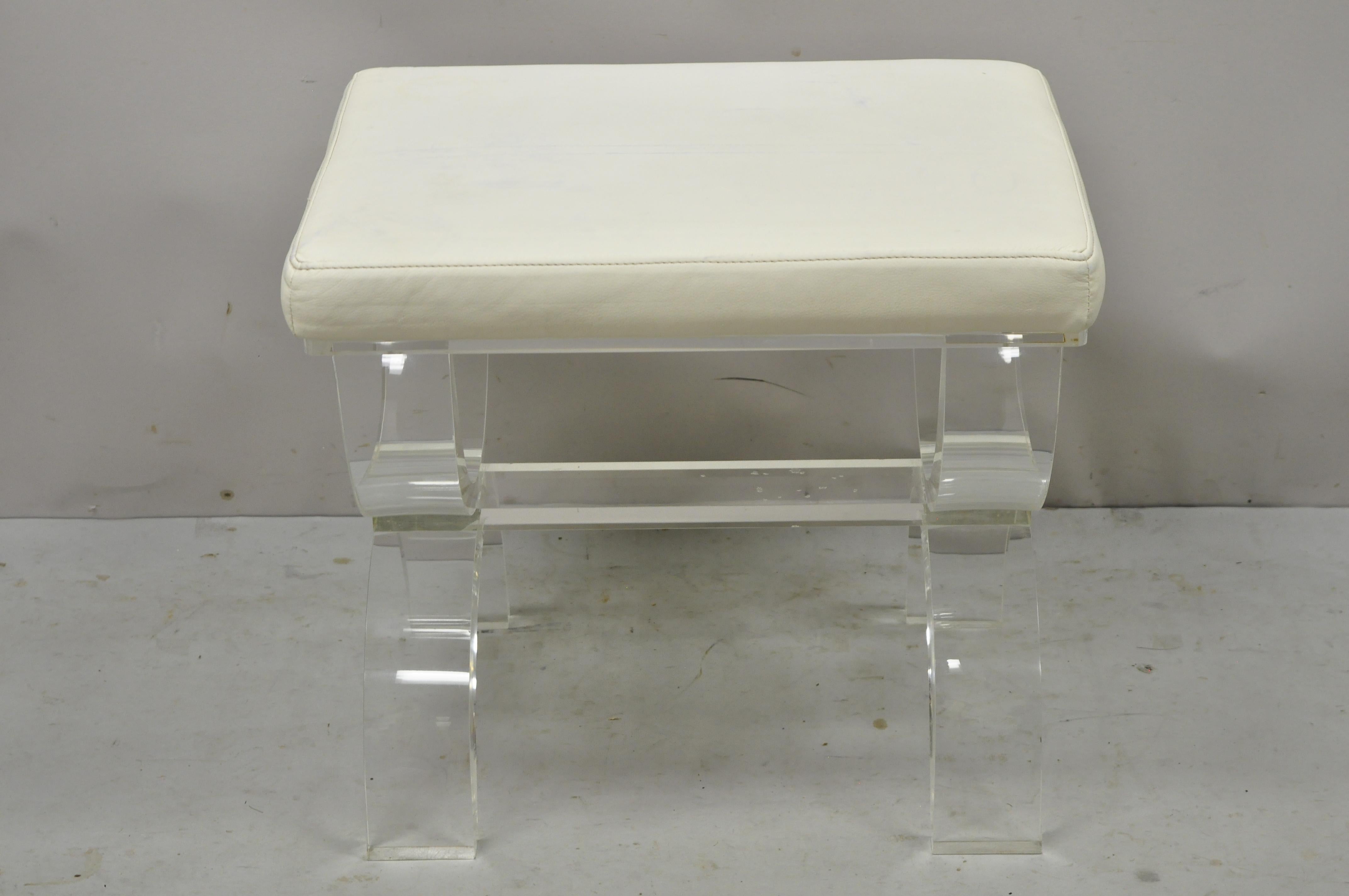 Modern clear lucite acrylic mid century style X-frame vanity bench stool. Item features heavy thick lucite sculptural base, white naugahyde upholstered seat, original label, quality craftsmanship, sleek sculptural form. Circa 21st century,
