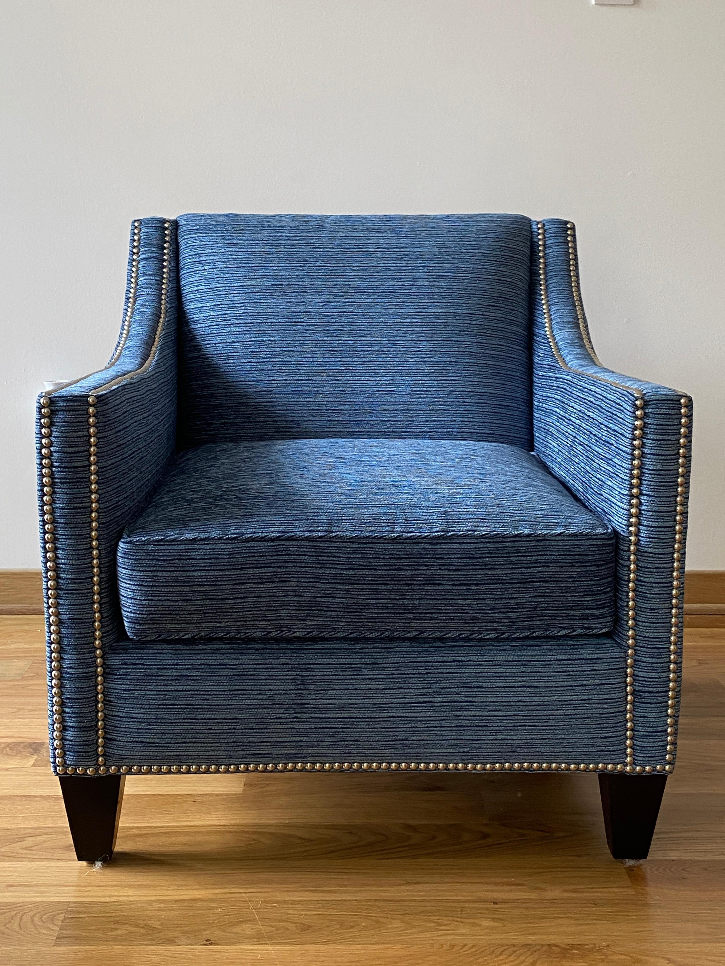 Listed is a modern, pair of custom, sloped-arm club chairs. The pair are upholstered in a soft, blended woven performance-fabric and complimented by polished nickel nailhead trim along the edges. The seat cushion is down wrapped foam-core. Dark