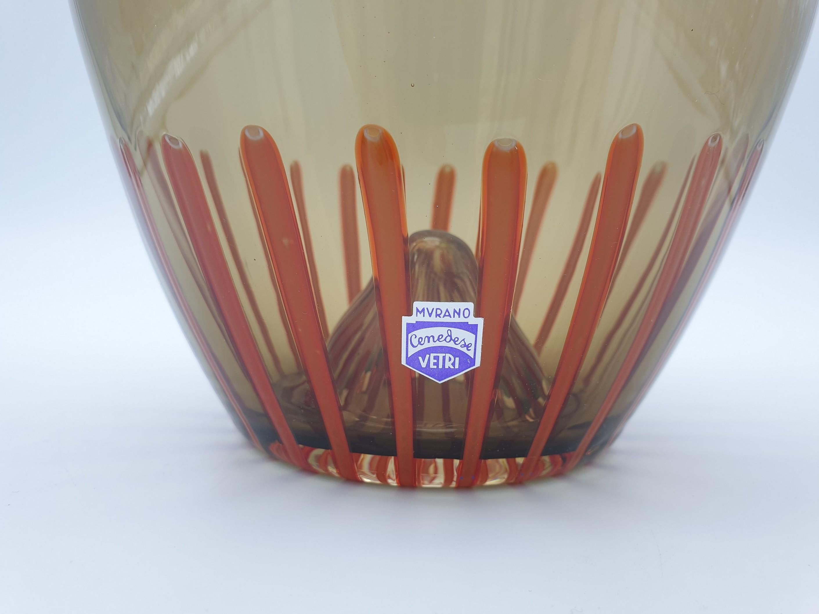 A bongo-drum shaped glass vase, handmade in Murano by Gino Cenedese e Figlio in the late 1990s. The warm coffee color and the delicate canes on its edges (mustard on the top and red on the bottom) recall to memory the beautiful sunsets of Africa, to