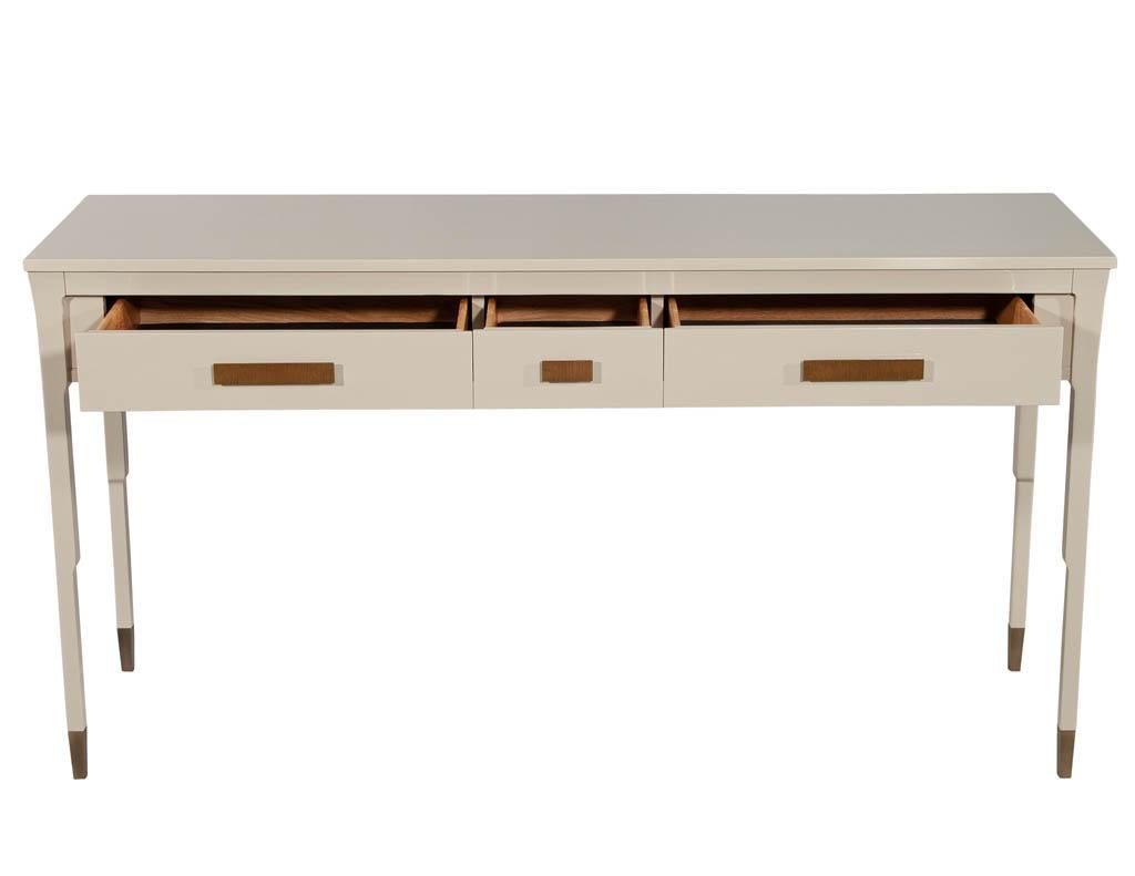 Modern console table hand polished lacquer. Beautiful hand polished lacquer finish with custom brass hardware. Unique sleek design with brass capped feet. Featuring 3 drawers for ample storage, all with lined with luxurious felt.