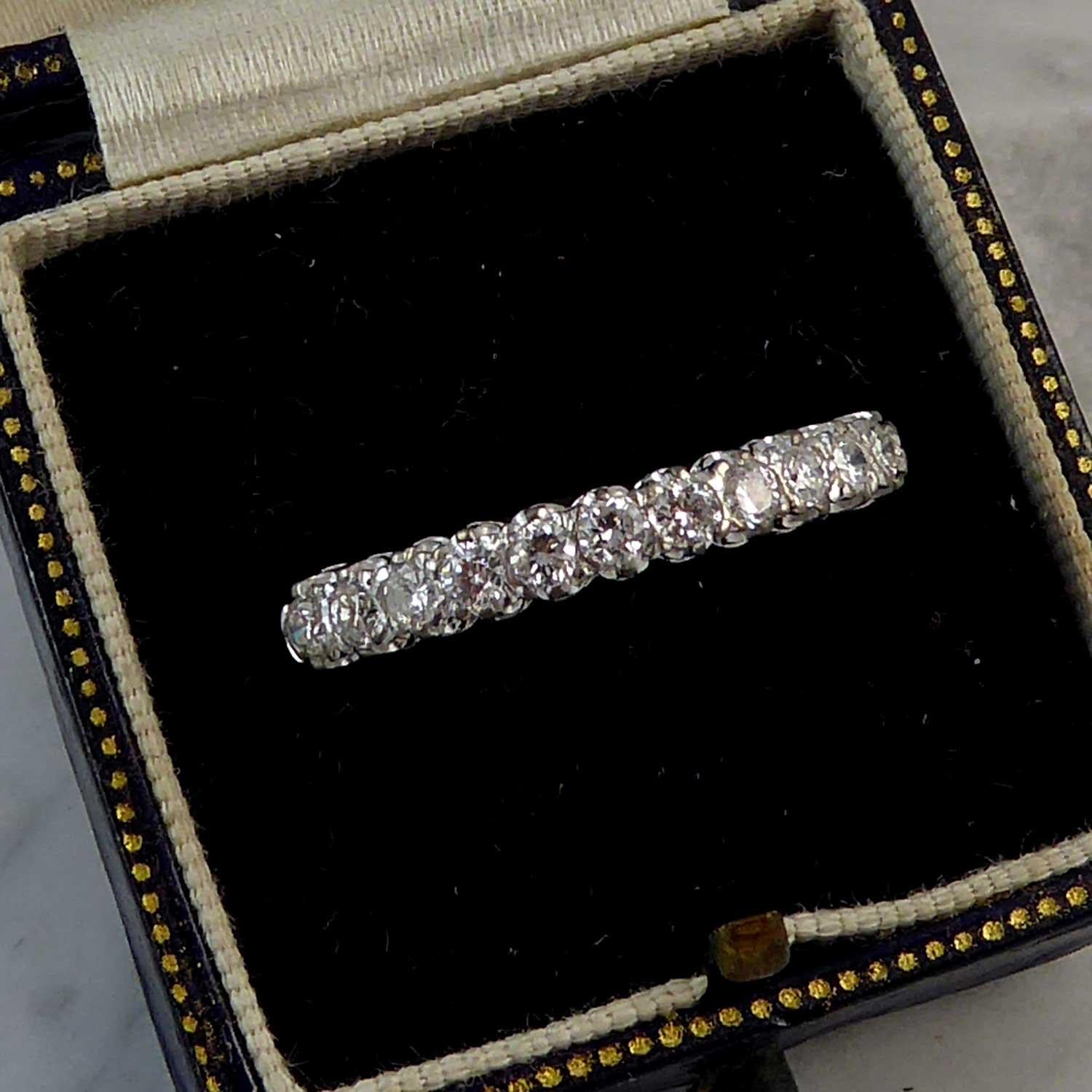 A contemporary diamond wedding or eternity ring set to the front half with 11 claw set brilliant cut diamonds, measuring approx. 2.1mm to 2.2mm in diameter, to a white uniform coronet style gallery with trefoil wire and grooved shoulders continuing