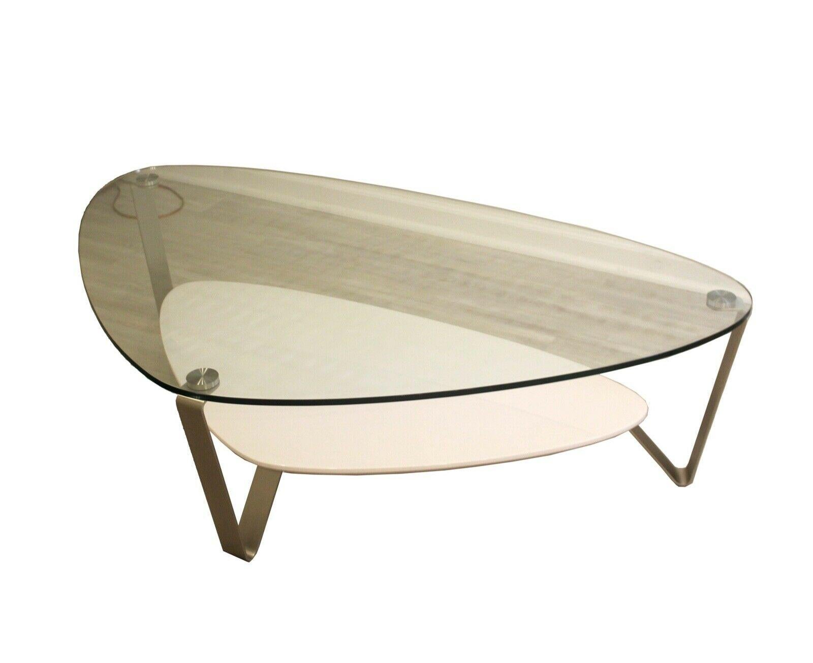 3 Legged contemporary coffee table with gloss white bottom shelf and glass top with polished metal legs. In excellent condition. Dimensions: 54.5 W X 33.25 D X 15.25 H.
 