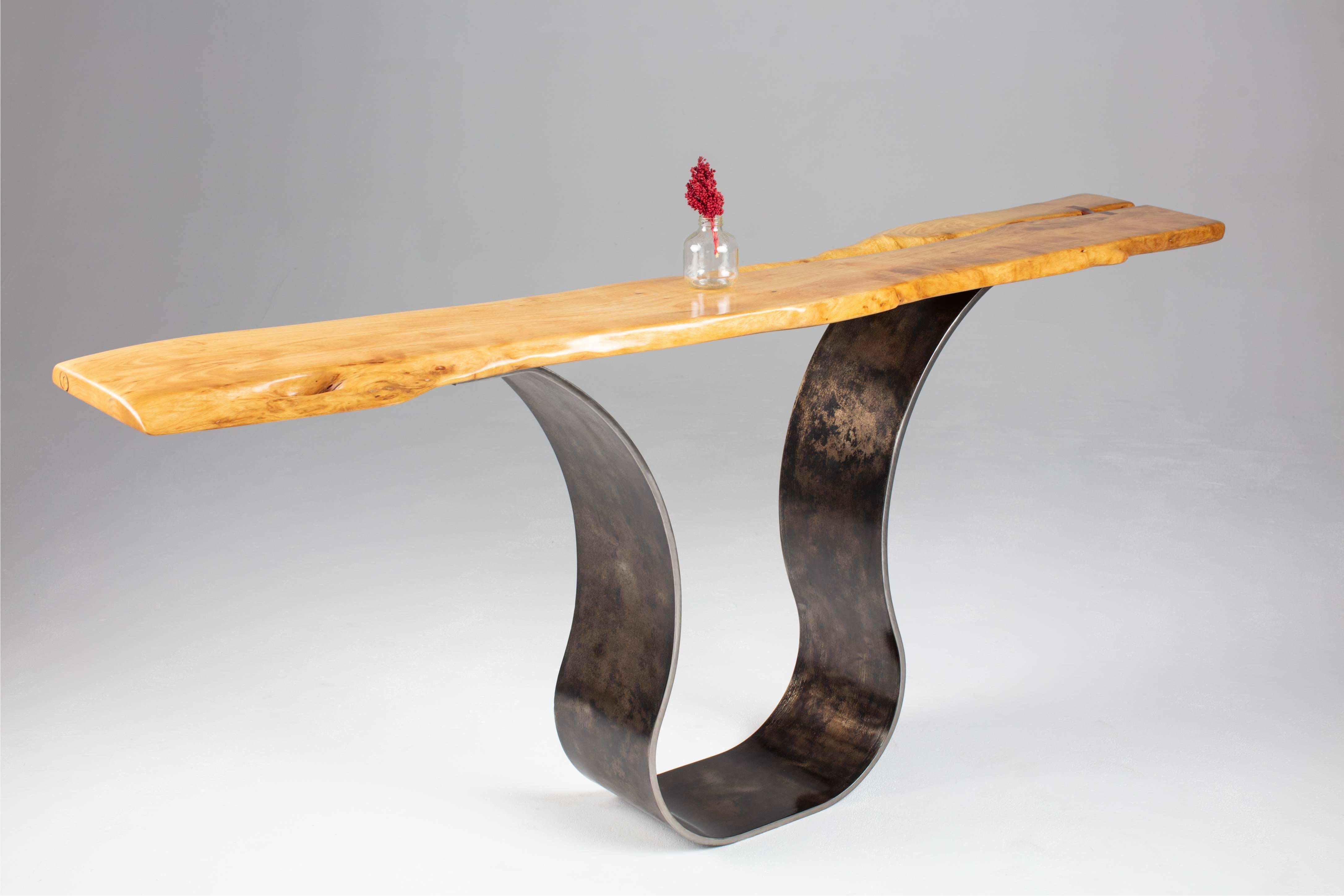Der Konsolentisch Tina von Carlo aus antikisiertem Stahl ist ein skulpturaler Eingangstisch, der modern-industrielle mit organischen Elementen verbindet. Eine handverlesene Platte mit lebendiger Kante wird sorgfältig geschliffen, bevor sie mit einer