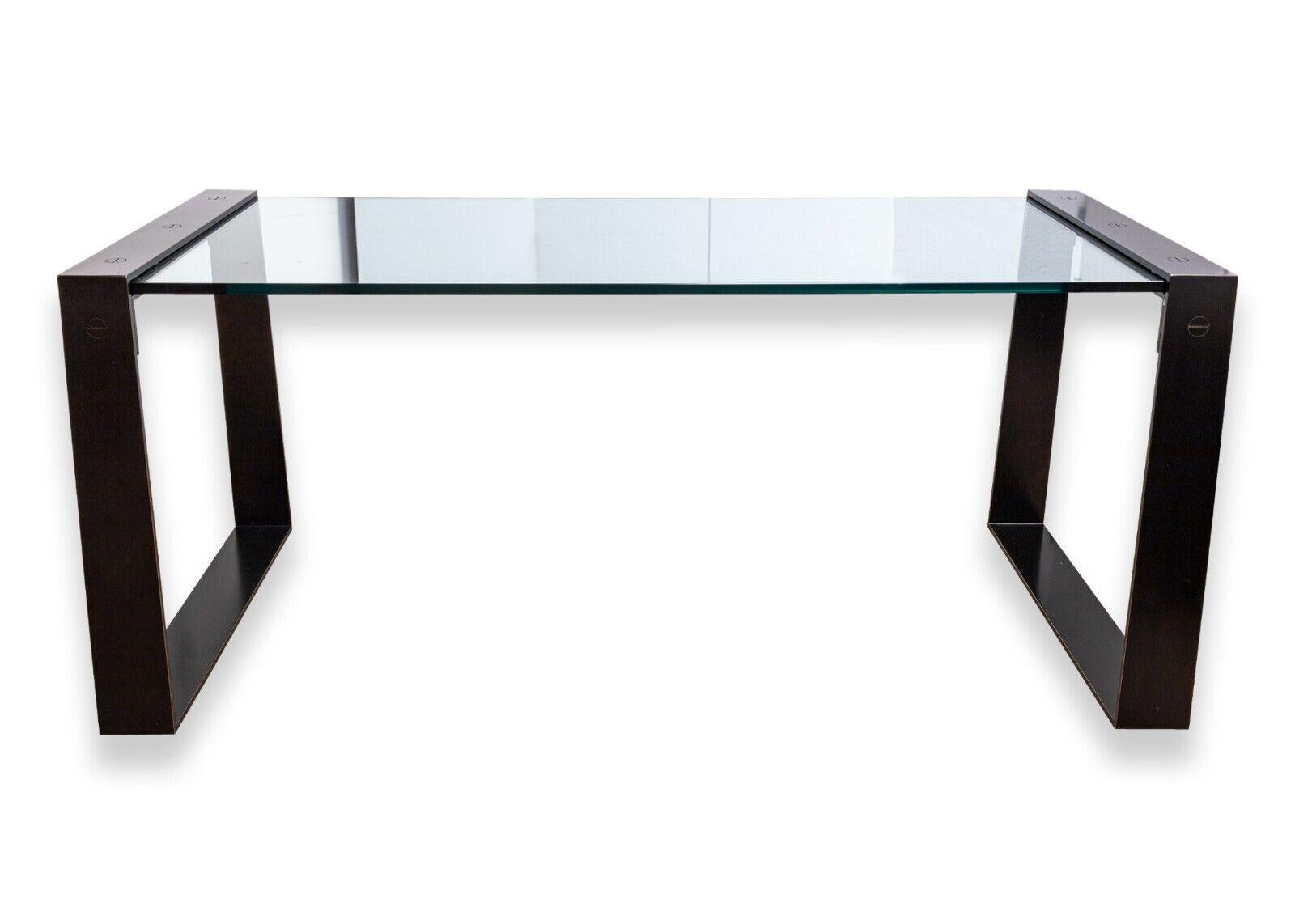 A modern contemporary Restoration Hardware glass desk. This magnificent desk from restoration hardware features a very modern design featuring a thick glass top that is supported by two black rounded rectangular legs on either side. The glass slips