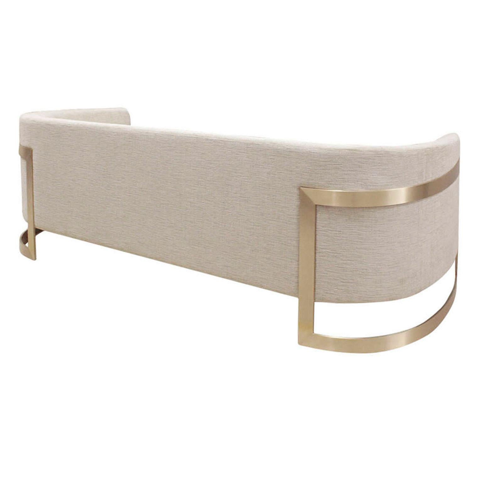 The contemporary sofa features a curved back and sleek metal frame. The upholstered body has a single seat cushion with three back cushions for comfort. The legs, shown in a brushed brass finish, wrap up and around the sides, supporting the
