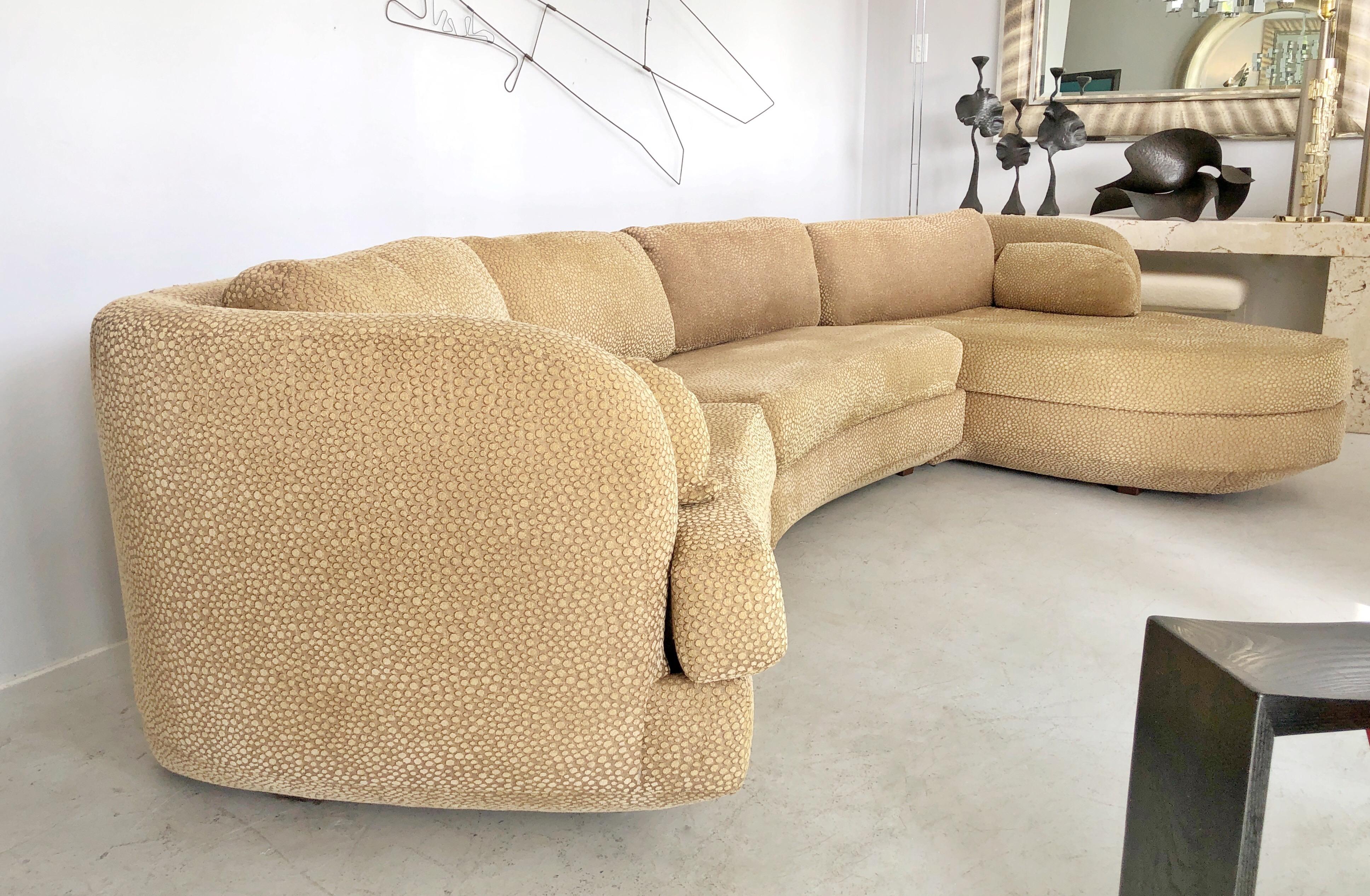 A curved sectional sofa. 3 pieces with one being an asymmetrical chaise. The bottom of the sofa angles back creating a floating visual sensation. Down pillows on back. Chaise length is 63”.