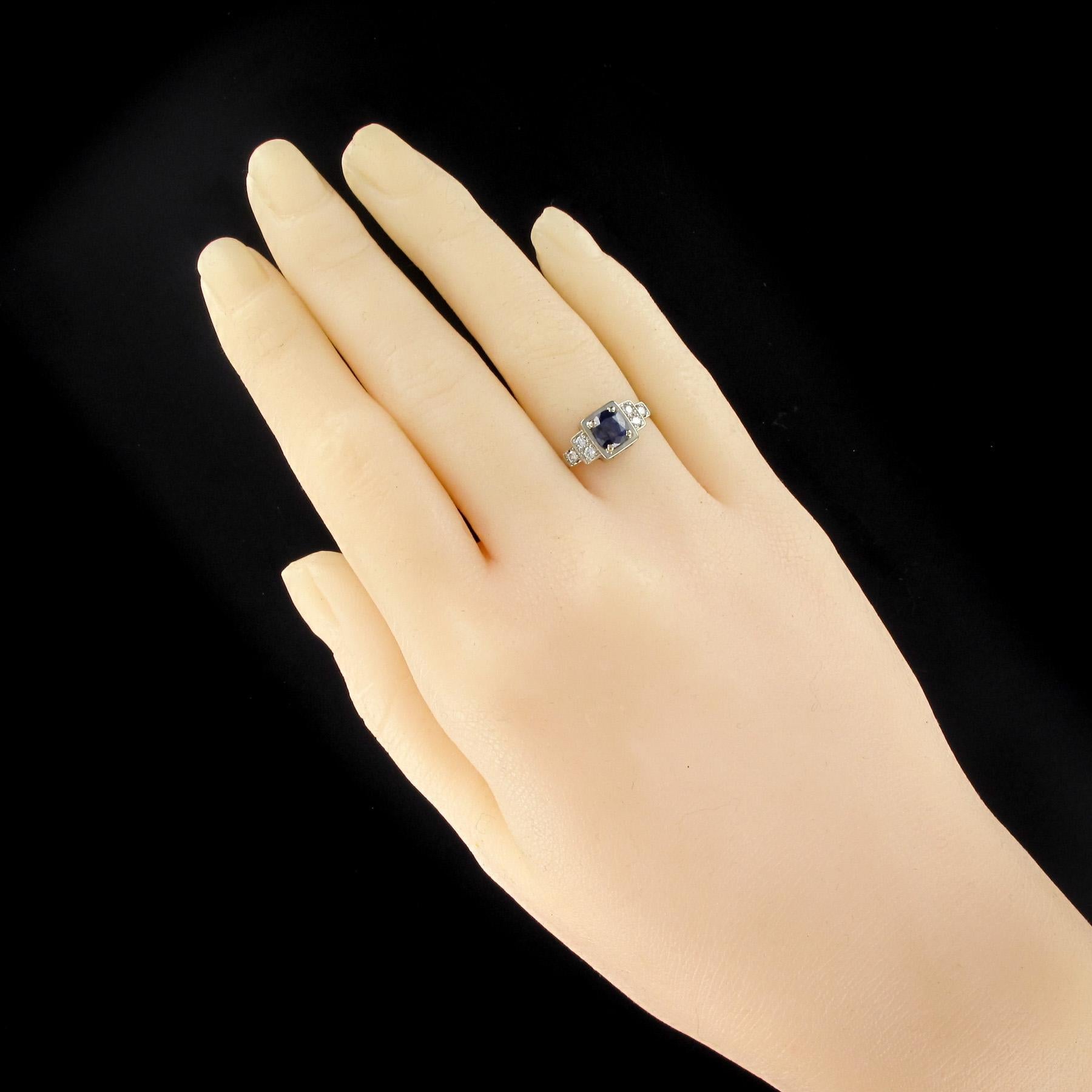 Ring in 18 karats white gold, eagle's head hallmark.
Art Deco style ring, this beautiful white gold ring is set with 4 claws on a rectangular set by a cushion cut sapphire of a beautiful deep blue and bright. On either side of the head are set 2 x 3
