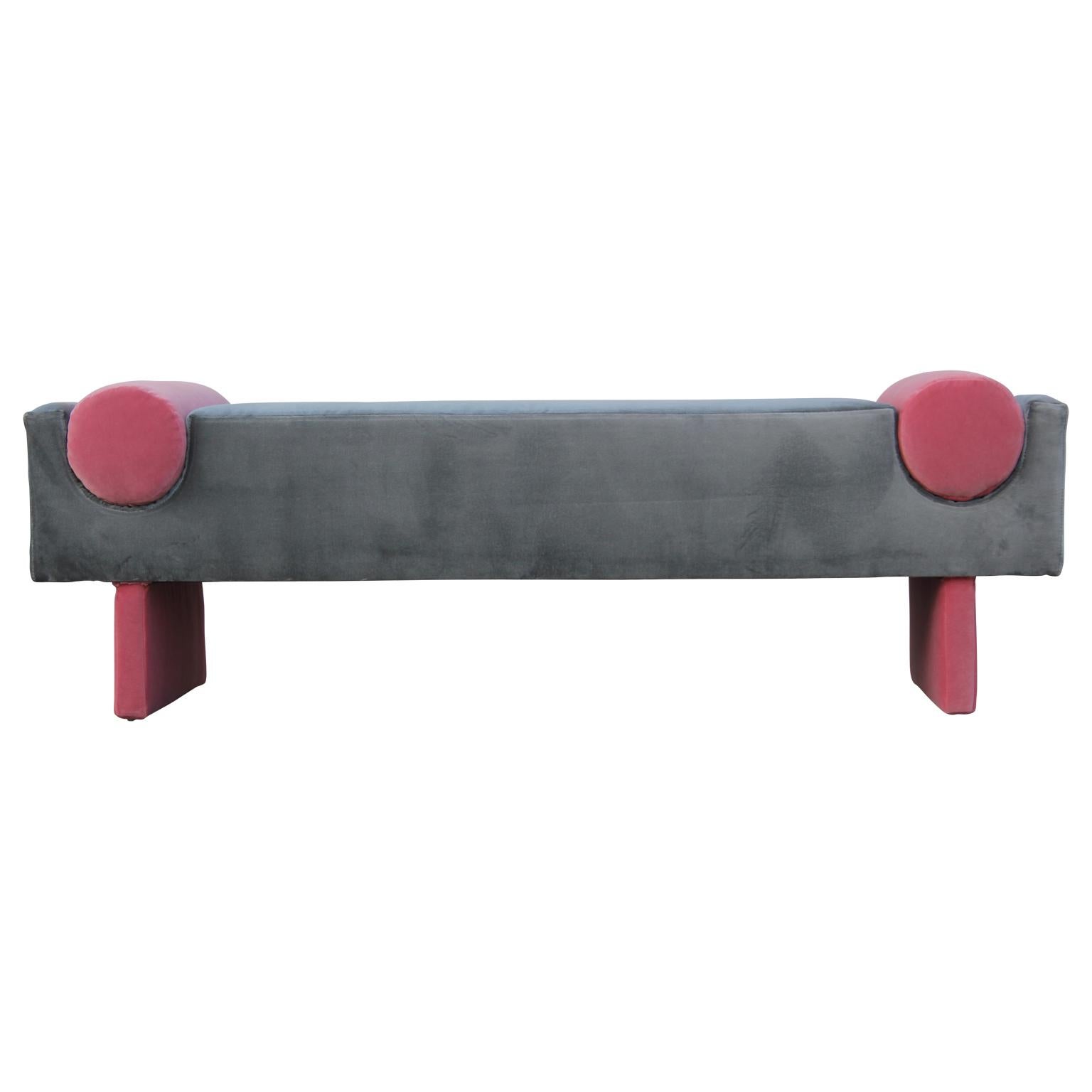 Custom-made bench upholstered in a rich dark grey velvet with pink velvet legs and matching pink velvet bolster accents that are attached.