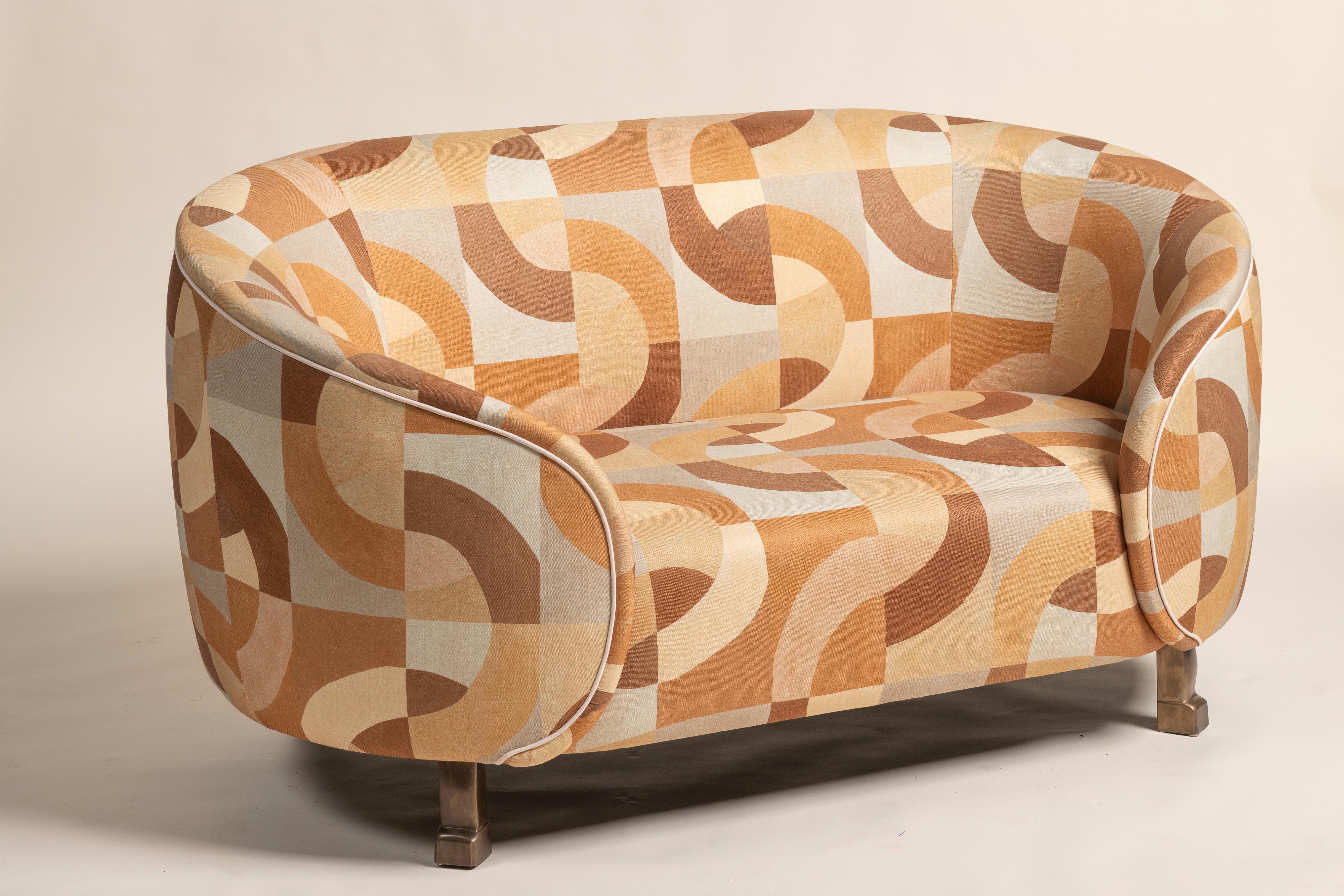 Custom settee upholstered in Kelly Wearstler linen with a modern geometric pattern in warm, earthy tones. The settee has a rounded, cozy form with curved arms and a smooth, continuous backrest, creating a soft and inviting silhouette. It stands on