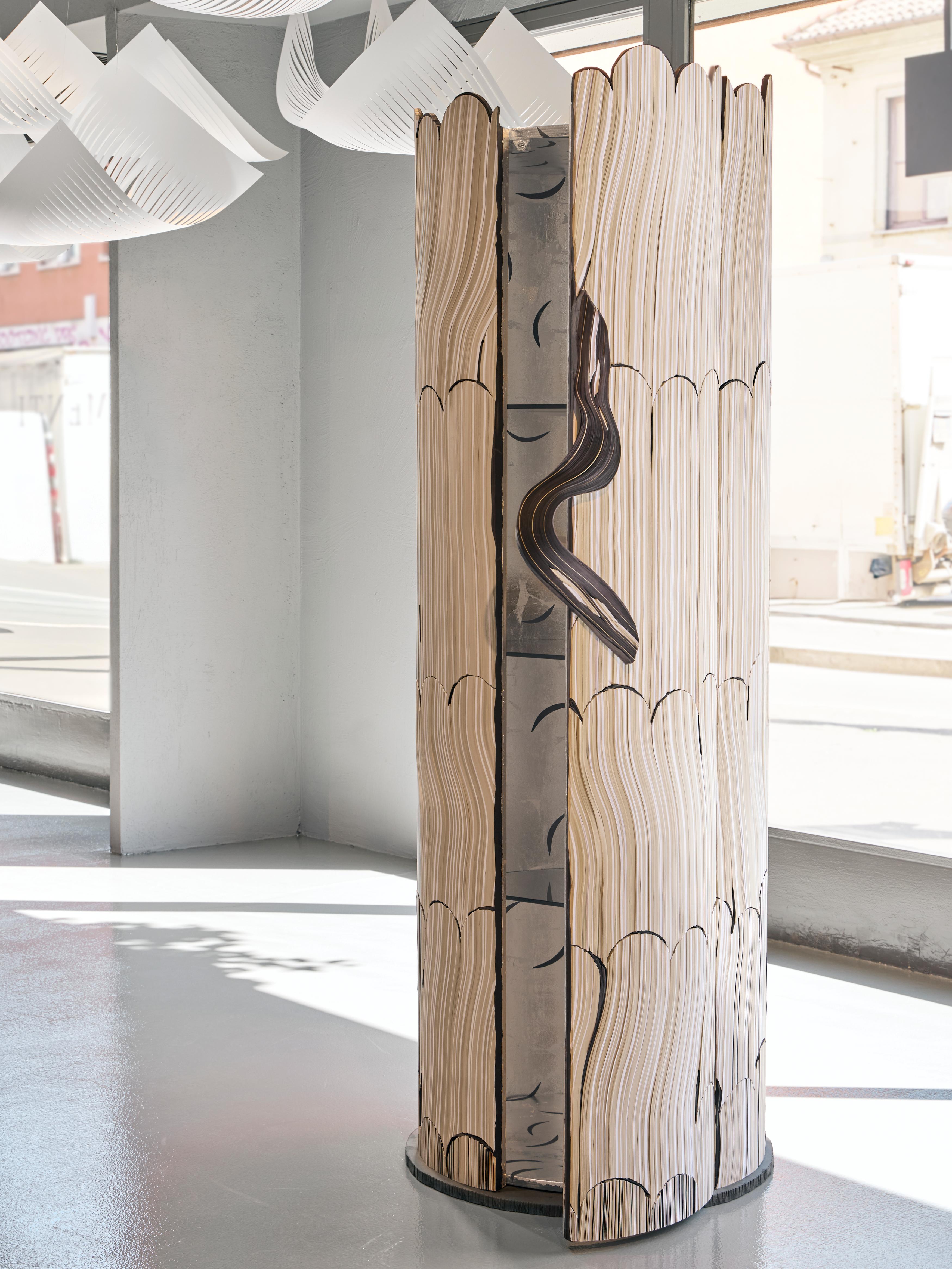 Cylindrical cabinet that develops vertically. The vertical and geometric rigor of the external inlay in grey tones contrasts with the decoration of the interior. A small black fragment, shaped sinuously, transformed into a handle that opens and