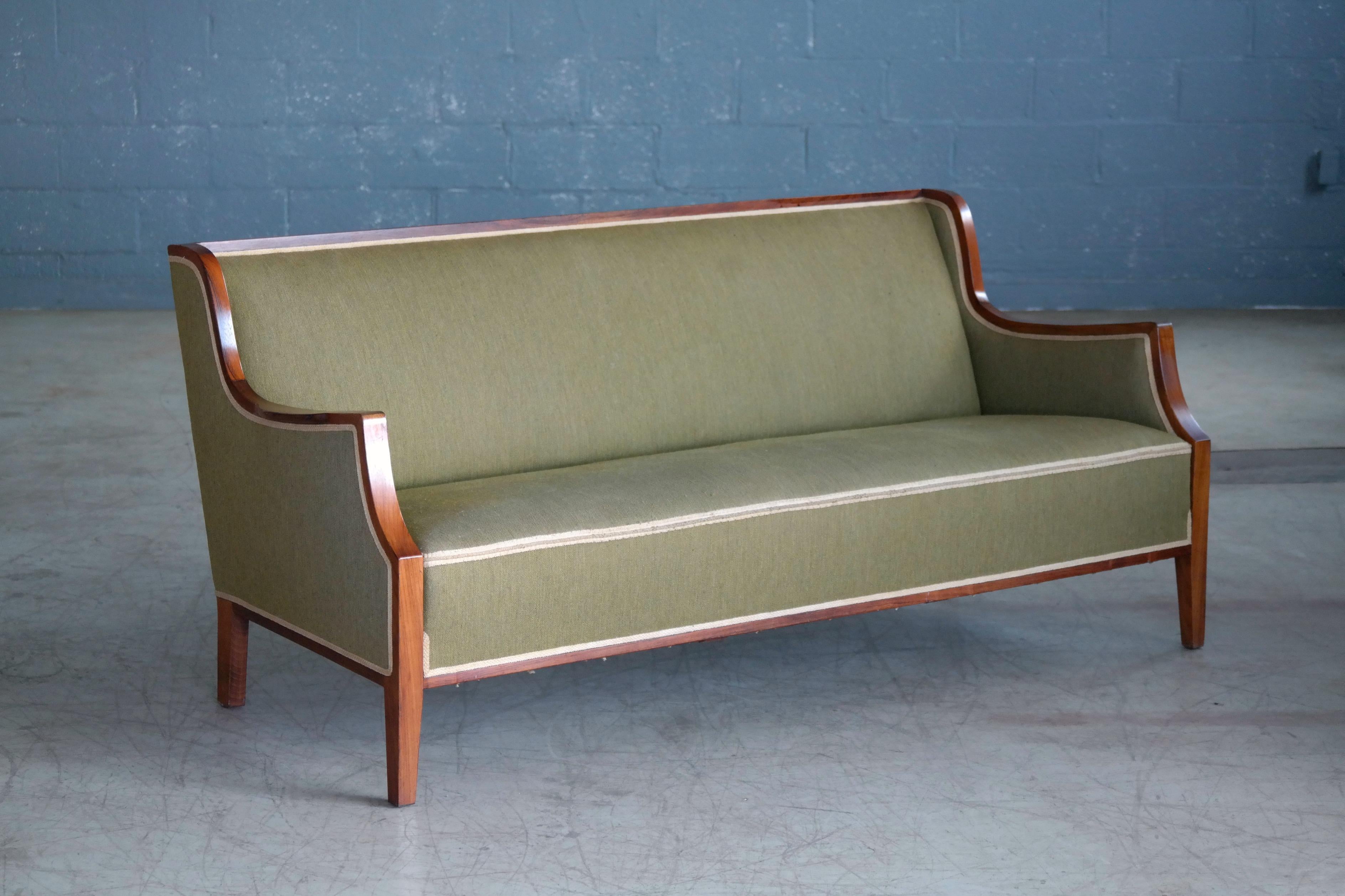 Frits Henningsen is famous for his Classic sofa designs with flared armrests and wooden frames extending into the tapered legs most of which were produced between 1935 and early 1940s. This sofa is a later and more modern version of his design
