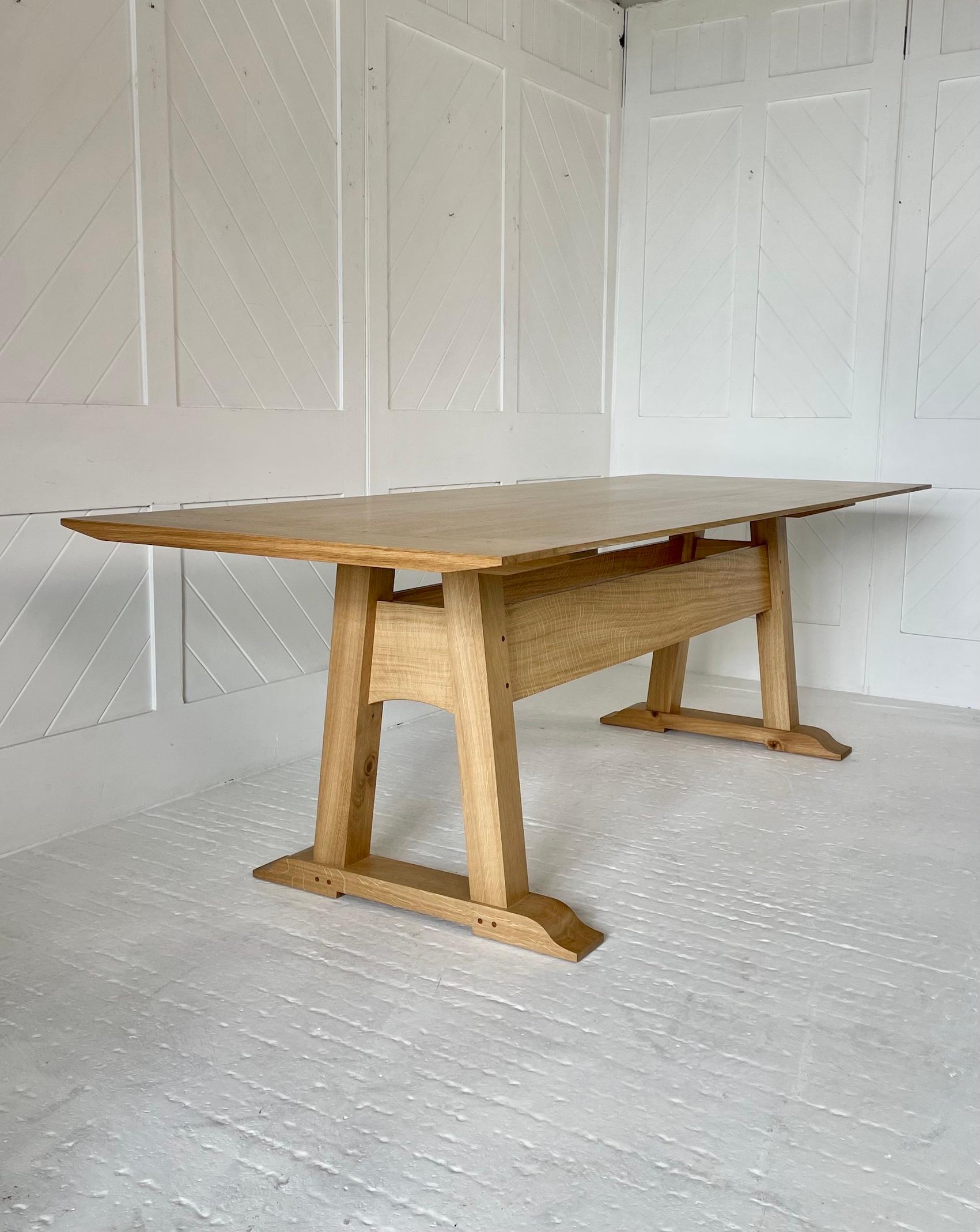 A 'Modern Day' 8 seater refectory table in lightly fumed English oak. .  Chamfered 3 plank solid quarter sawn oak top with cleated ends and pegged brown-oak dowels.

Three-quarter height full length stretchers. 

Trapezium shaped ends, curved rail