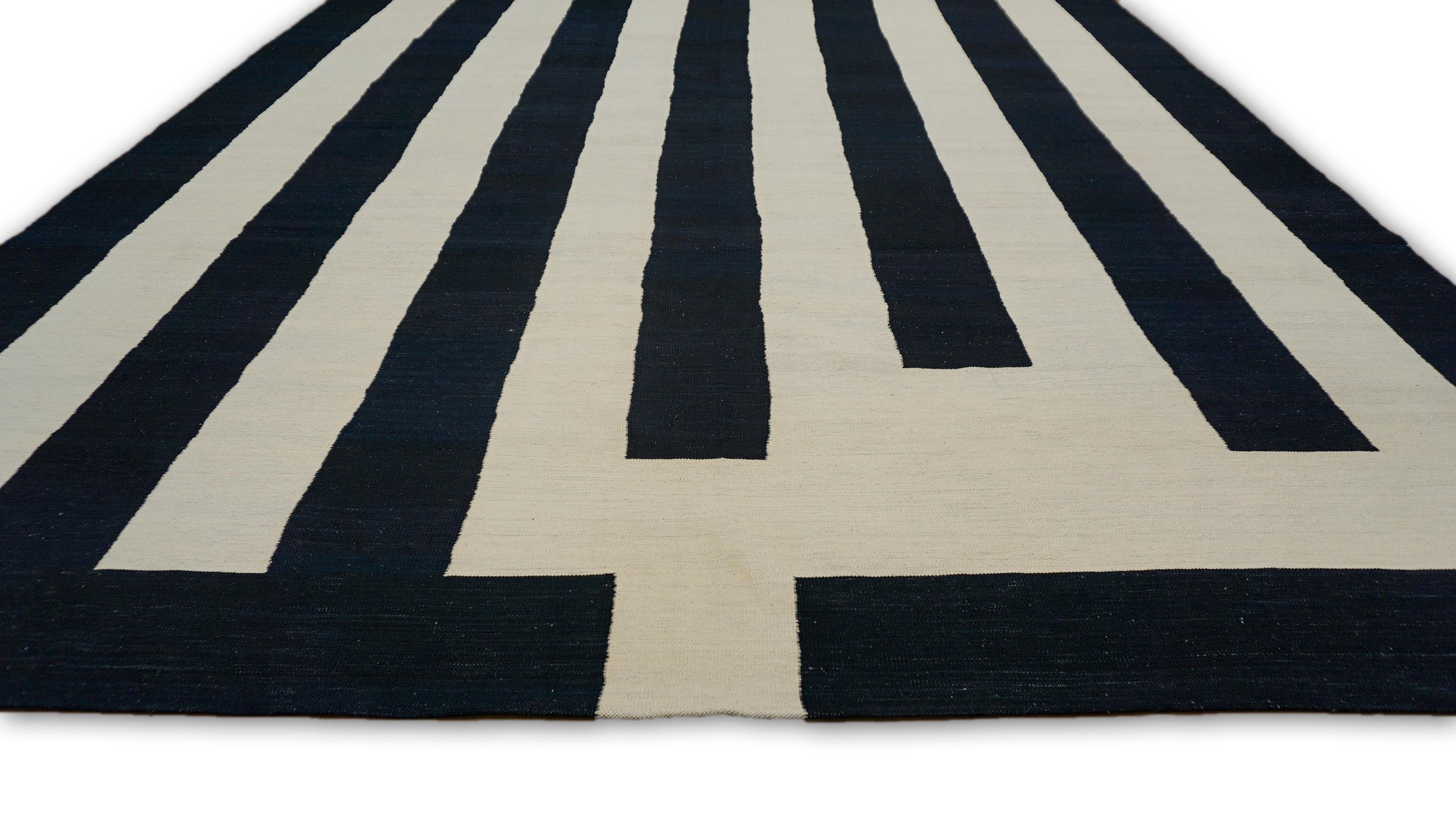 Esta lana tejida a mano  es un sorprendente ejemplo de minimalismo moderno y arte óptico. Con un atrevido motivo geométrico lineal en negro y marfil, esta alfombra crea una textura visual cautivadora, que la convierte en una pieza perfecta para