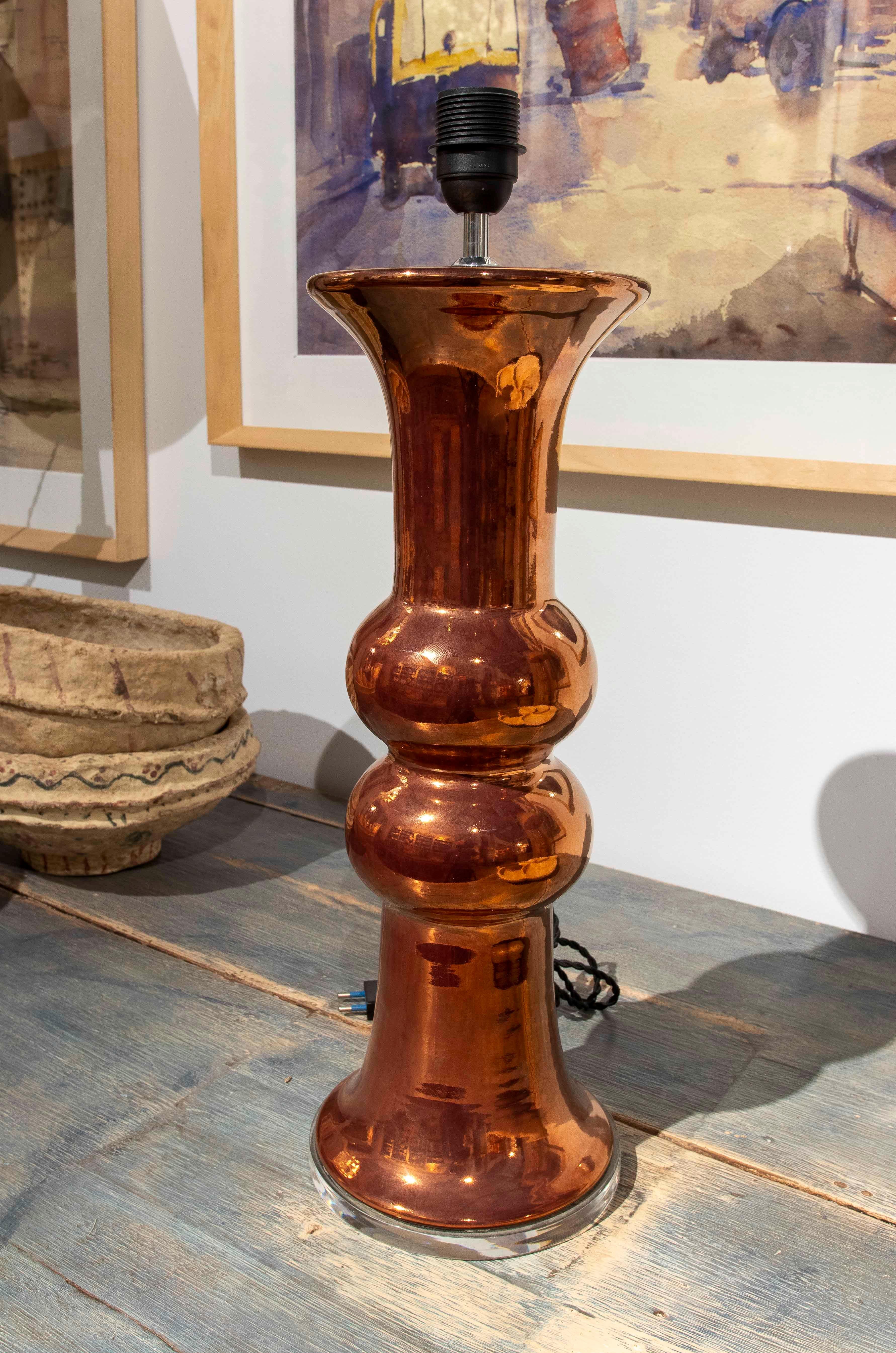 Elegant table lamp with a ceramic body in a copper finish, showcasing a contemporary and minimalist design. Its sculpted structure with curved and tiered shapes exudes sophistication, making it ideal for modern or industrial interiors. The glossy