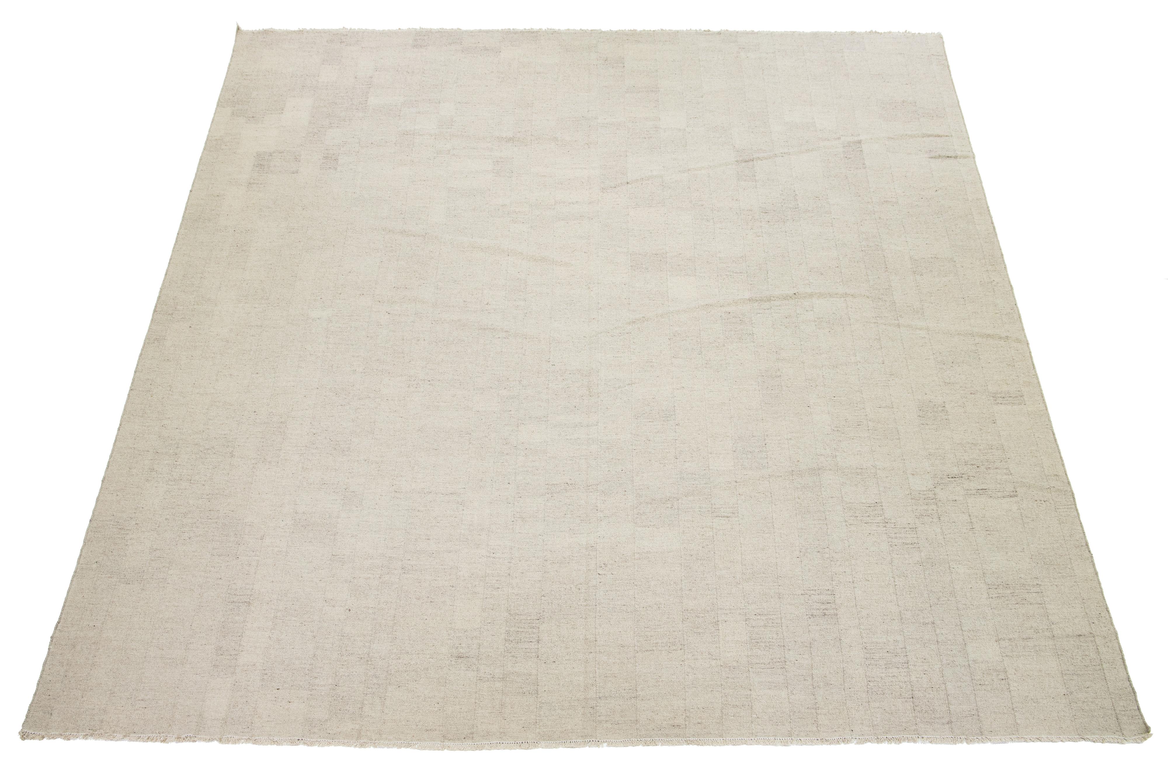 Dieser Teppich zeigt einen prächtigen zeitgenössischen flachgewebten Kilim im organischen Stil, der aus hochwertiger Wolle gefertigt ist. Seine beigefarbene Farbgebung strahlt Eleganz aus, die durch ein fesselndes geometrisches Muster ergänzt wird,