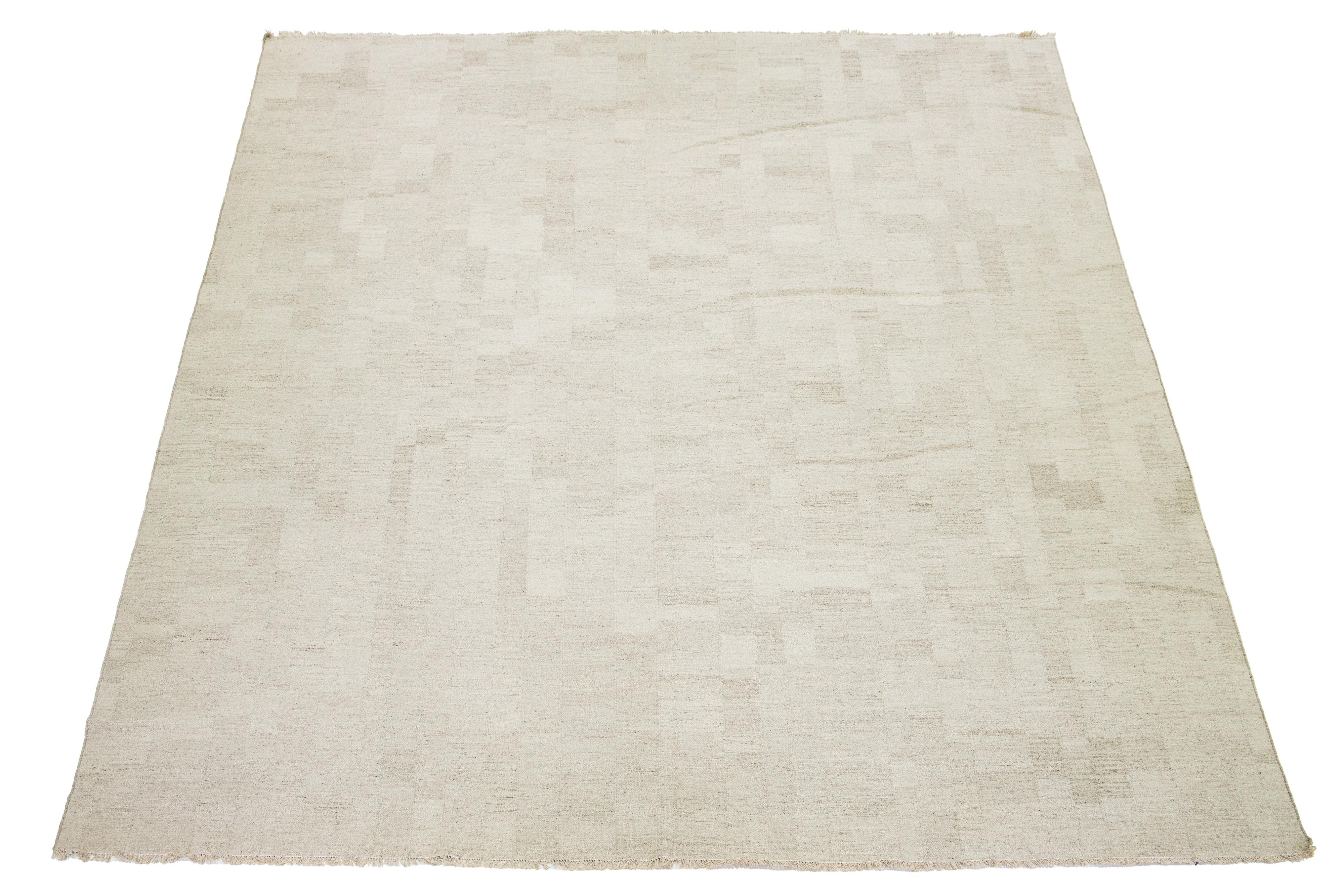 Dieser Teppich zeigt einen prächtigen zeitgenössischen flachgewebten Kilim im organischen Stil, der aus hochwertiger Wolle gefertigt ist. Seine beigefarbene Farbgebung strahlt Eleganz aus, die durch ein fesselndes geometrisches Muster ergänzt wird,