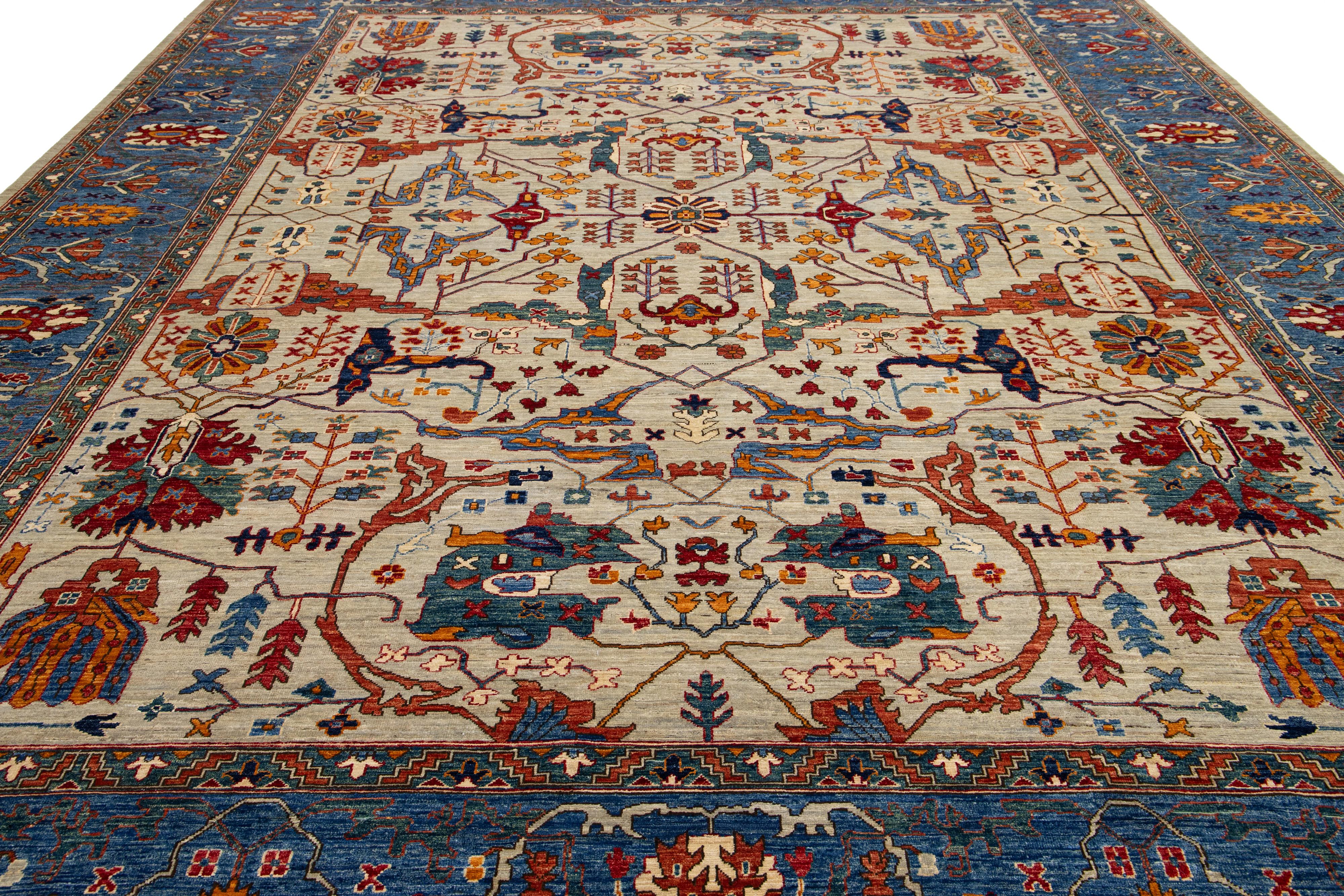Esta preciosa alfombra del tamaño de una habitación presenta una interpretación moderna del estilo clásico Serapi, elaborada con lana de alta calidad. Tiene un rico fondo beige con un borde azul, elegantemente adornado con un diseño floral