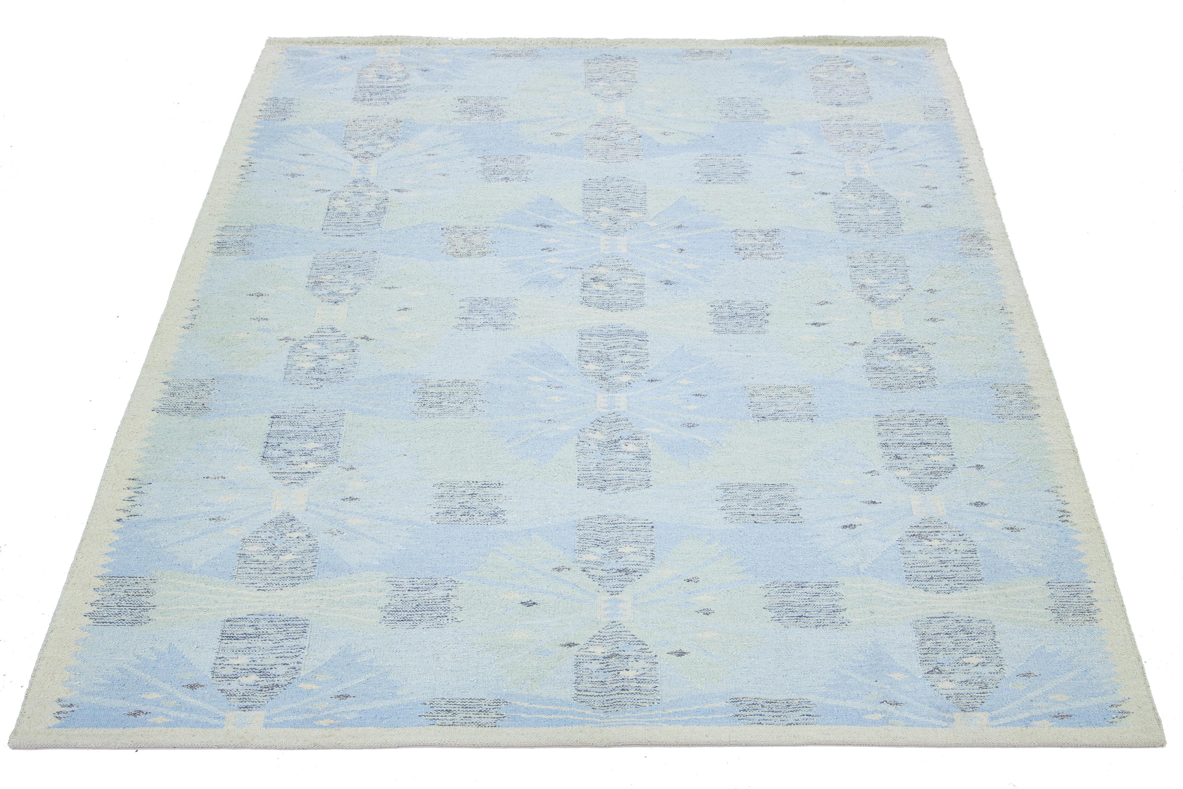 Dieser flachgewebte Teppich aus Wolle und Seide zeichnet sich durch ein schickes, modernes schwedisches Design mit einer beigen Feldfarbe aus. Der Teppich hat ein einzigartiges geometrisches Muster in hellblauen Farbtönen.

 Dieser Teppich misst 9'