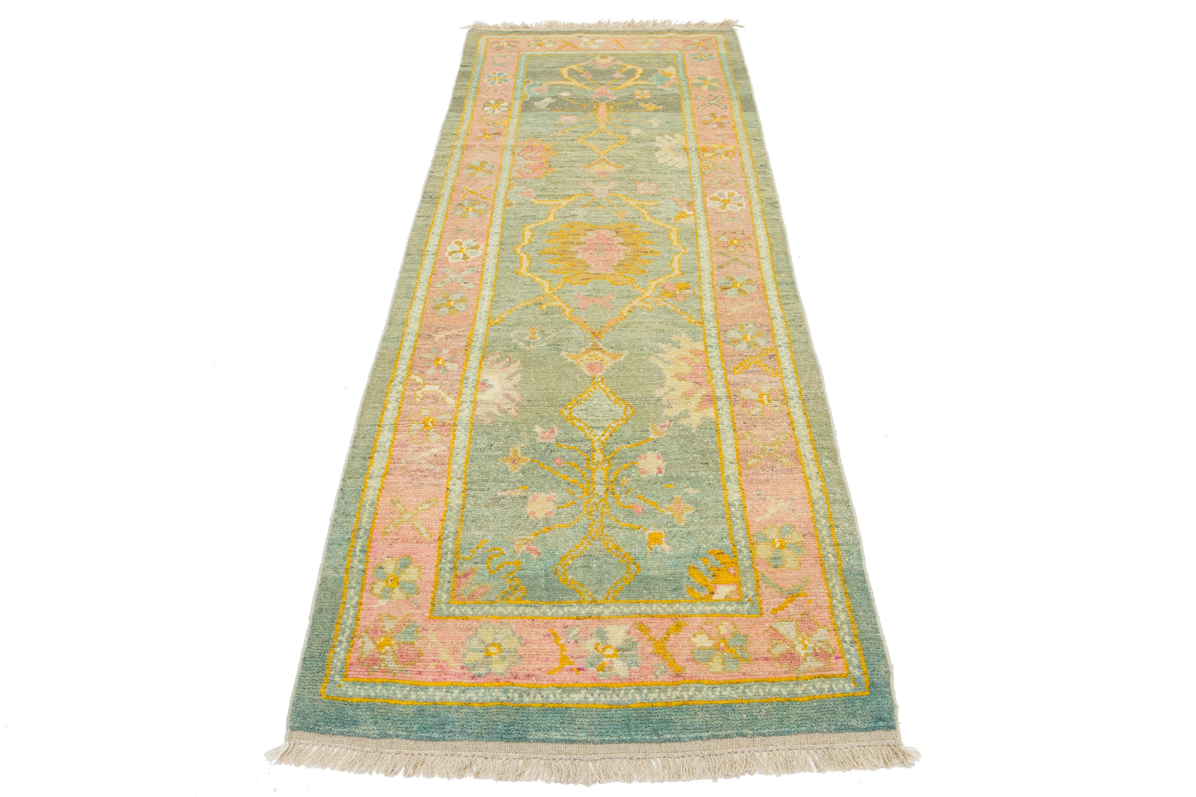 Beautiful modern Oushak hand-knotted wool rug with a green color field. This Turkish Piece has a pink frame with yellow, orange, pink, and green accent colors in a gorgeous all-over floral design.

This rug measures 3'1
