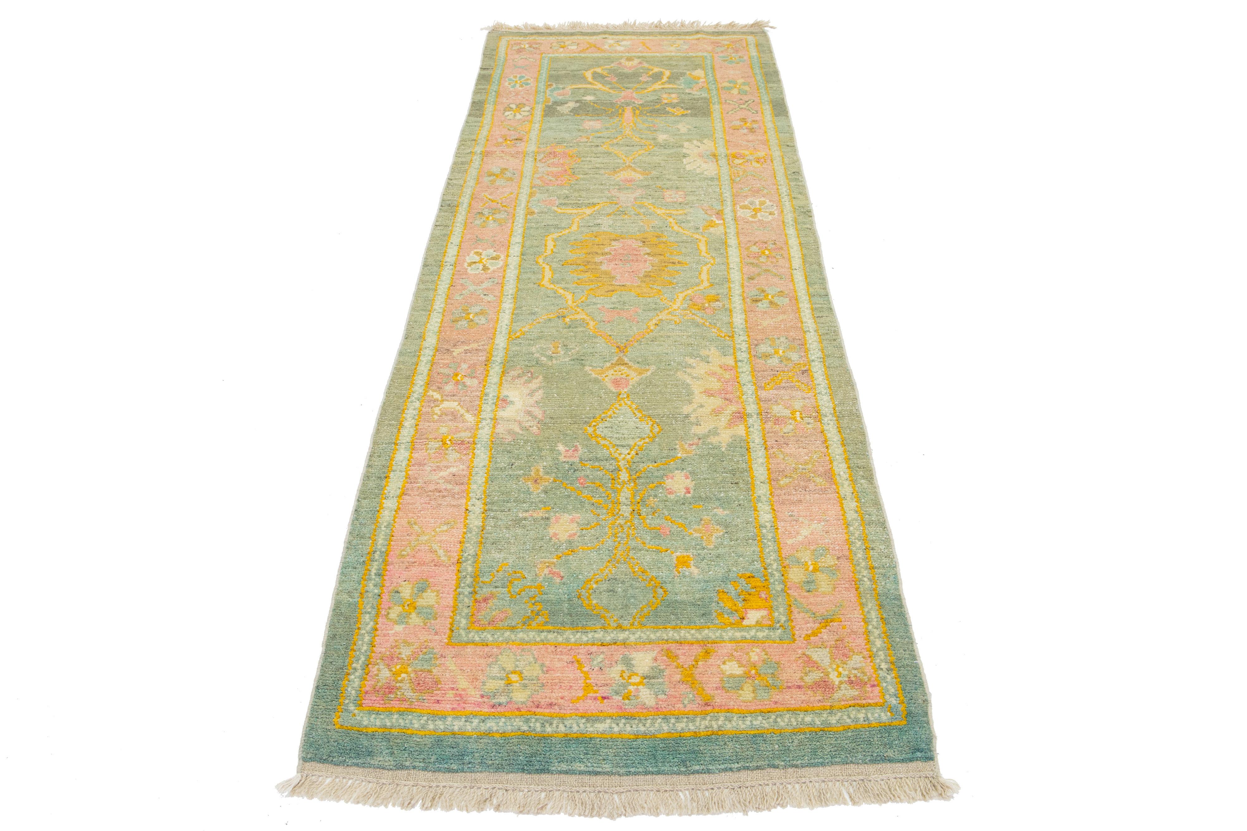 Bellissimo tappeto moderno in lana Oushak annodato a mano con un campo di colore verde. Questo pezzo turco ha una cornice rosa con accenti gialli, arancioni, rosa e verdi in uno splendido disegno floreale all-over.

Questo tappeto misura 3'1