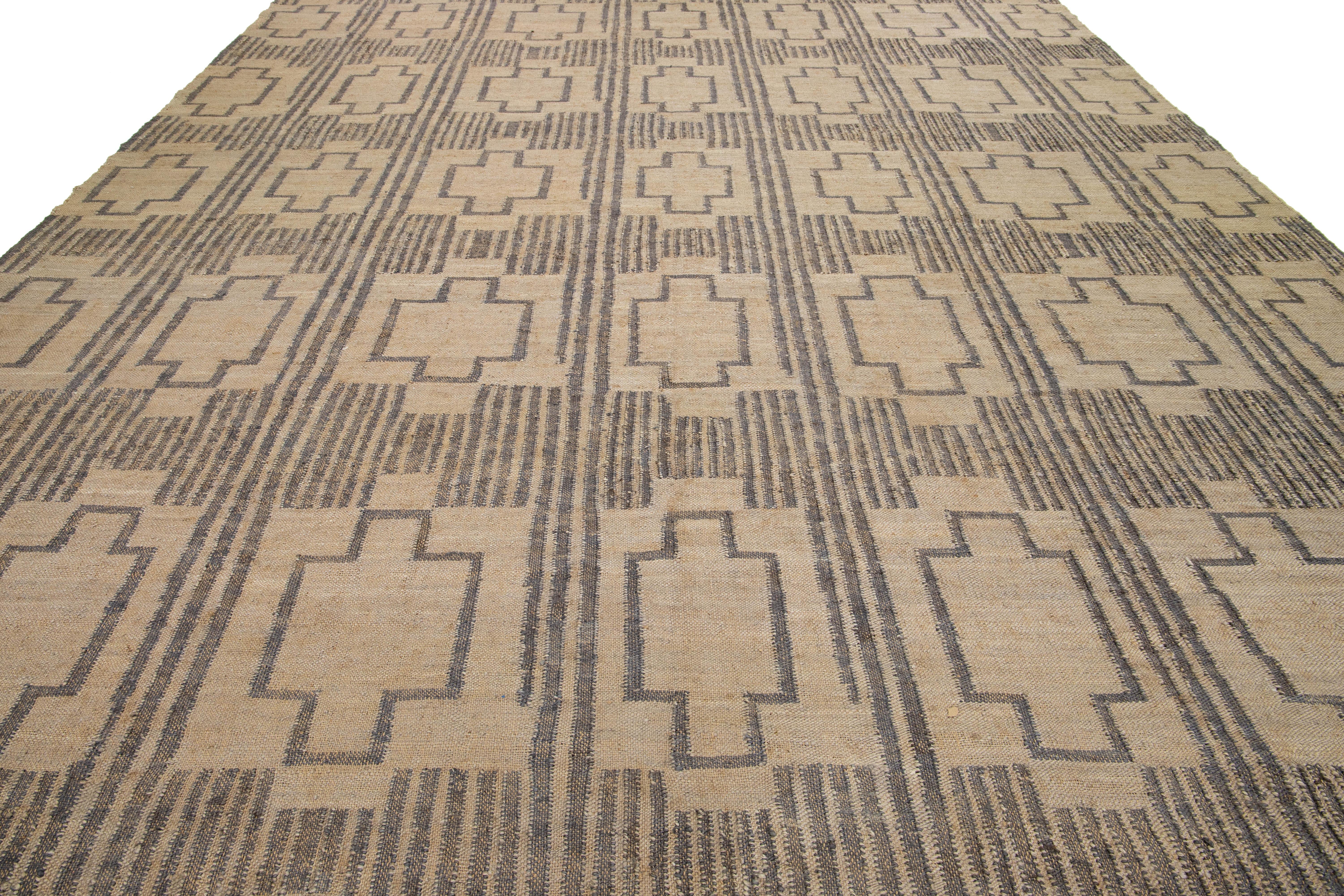 This flatweave natural jute rug showcases a contemporary Dhurrie design, featuring a tan-beige base color and stylish gray geometric accents.

 This rug measures 12'9
